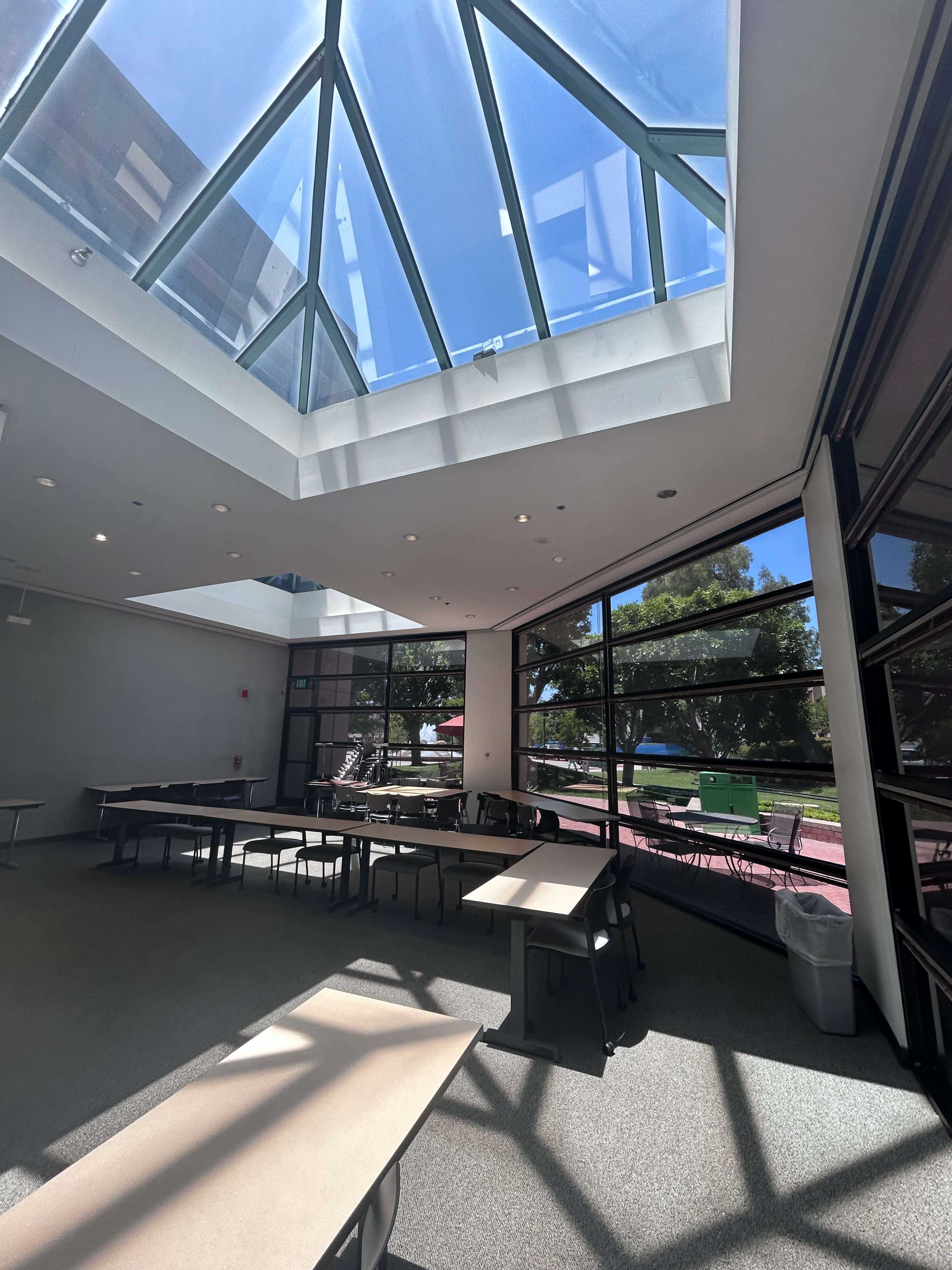 A bright, modern room with large windows and a skylight, featuring several tables arranged for use.
