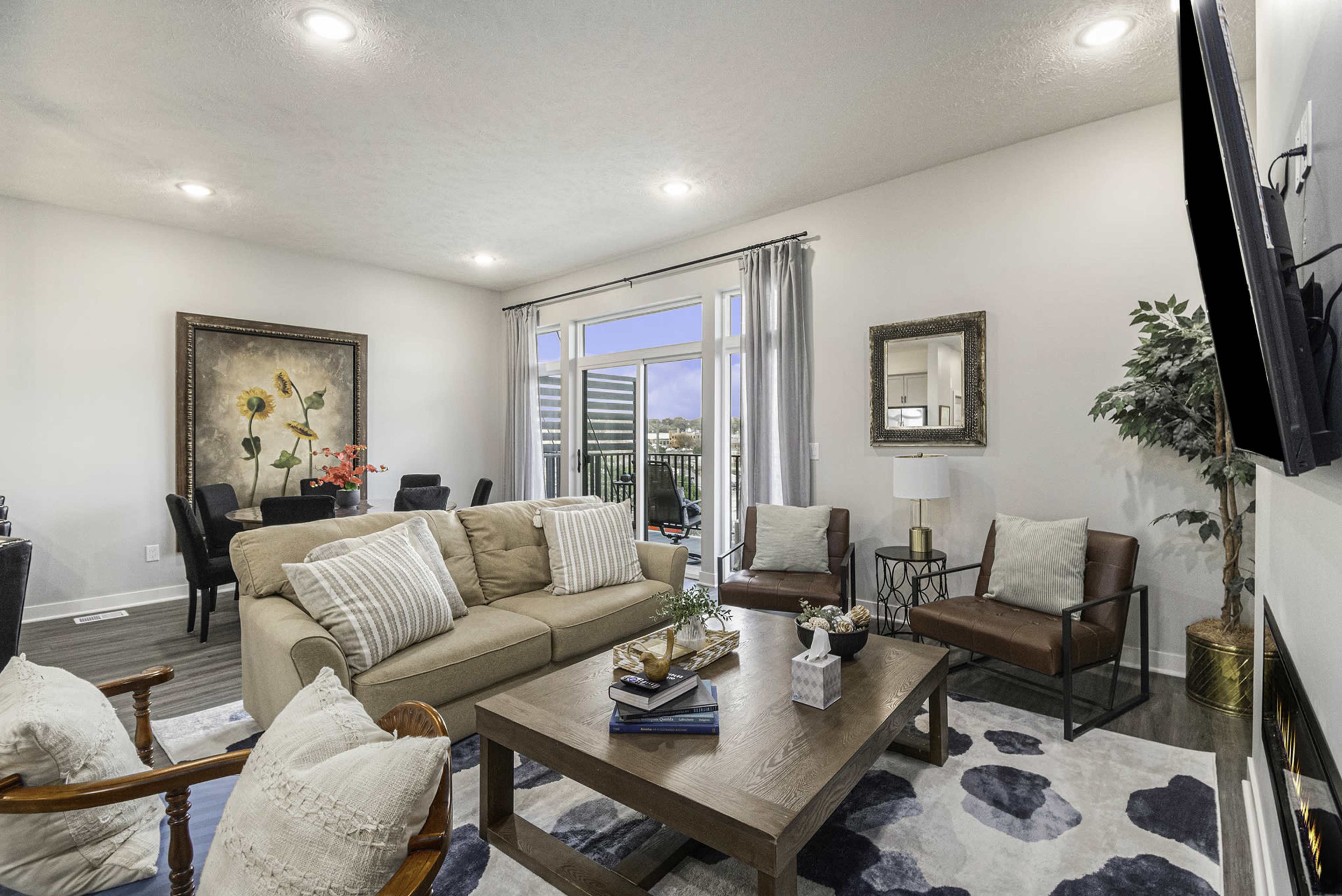 A modern living room features a beige sofa, a wooden coffee table, and large windows that open to a balcony view.