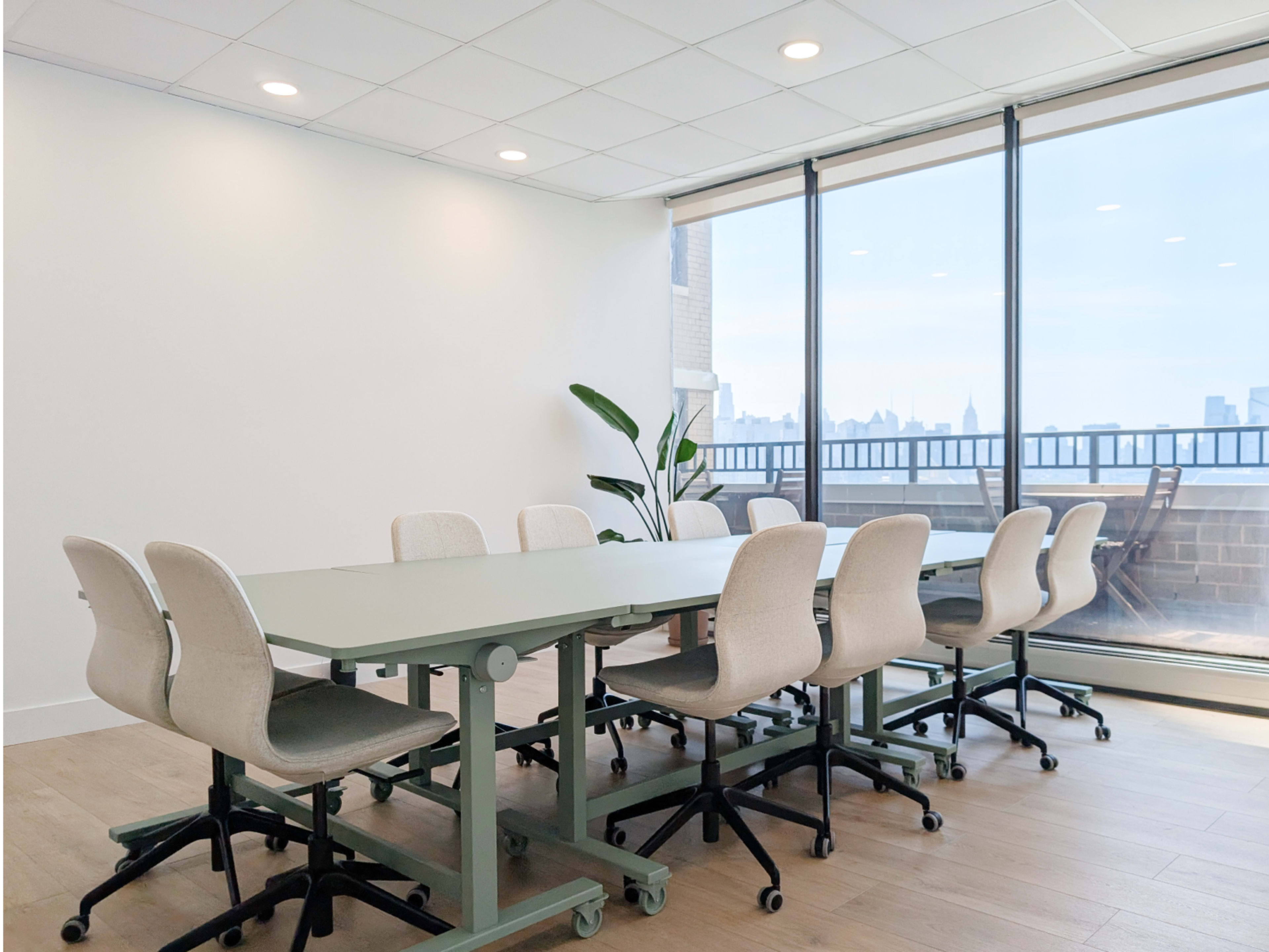 A modern conference room features a long table surrounded by rolling chairs, with large windows offering a view of the city skyline.