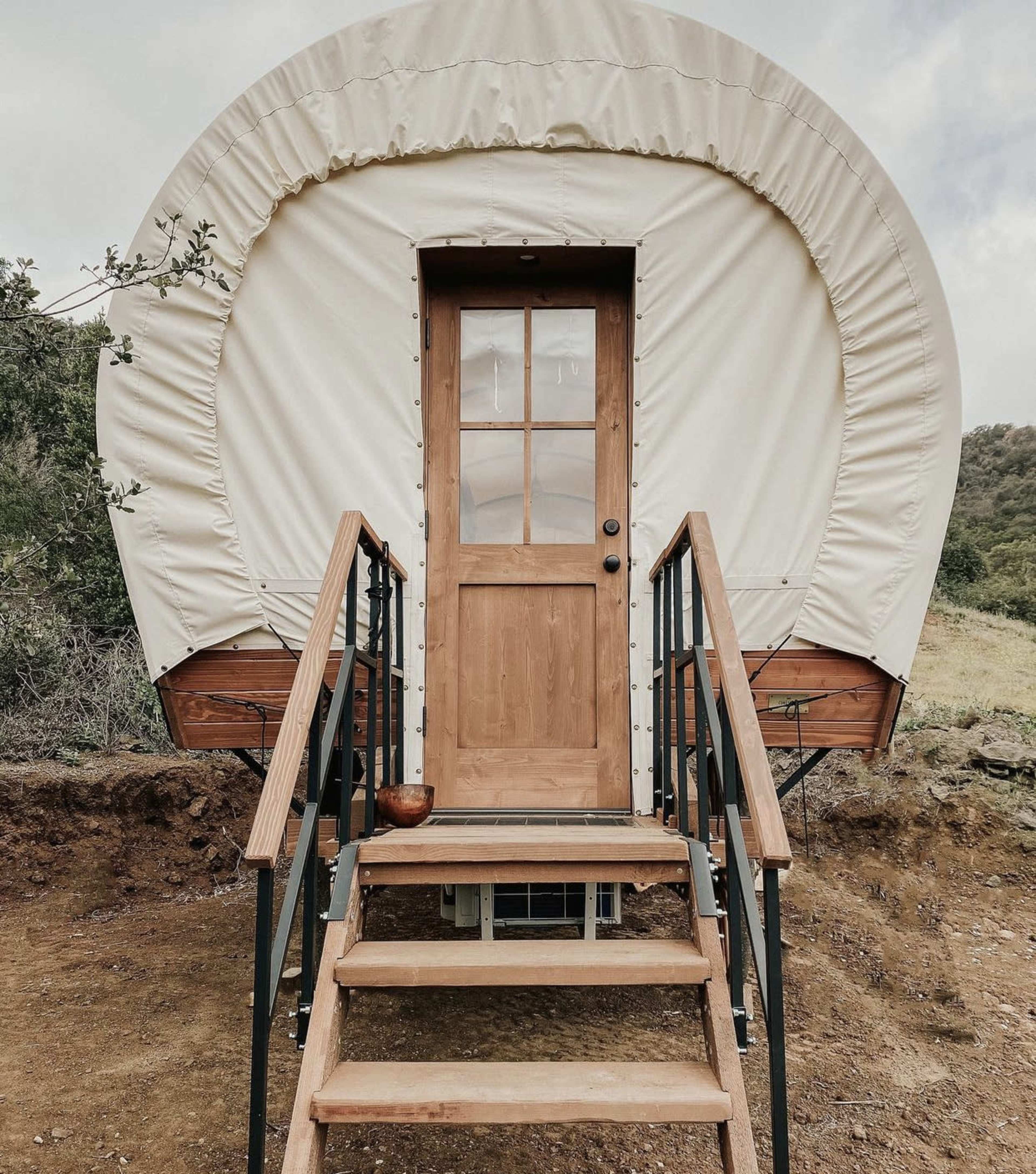 A round, canvas-covered structure with a wooden door and steps leads up to its entrance.