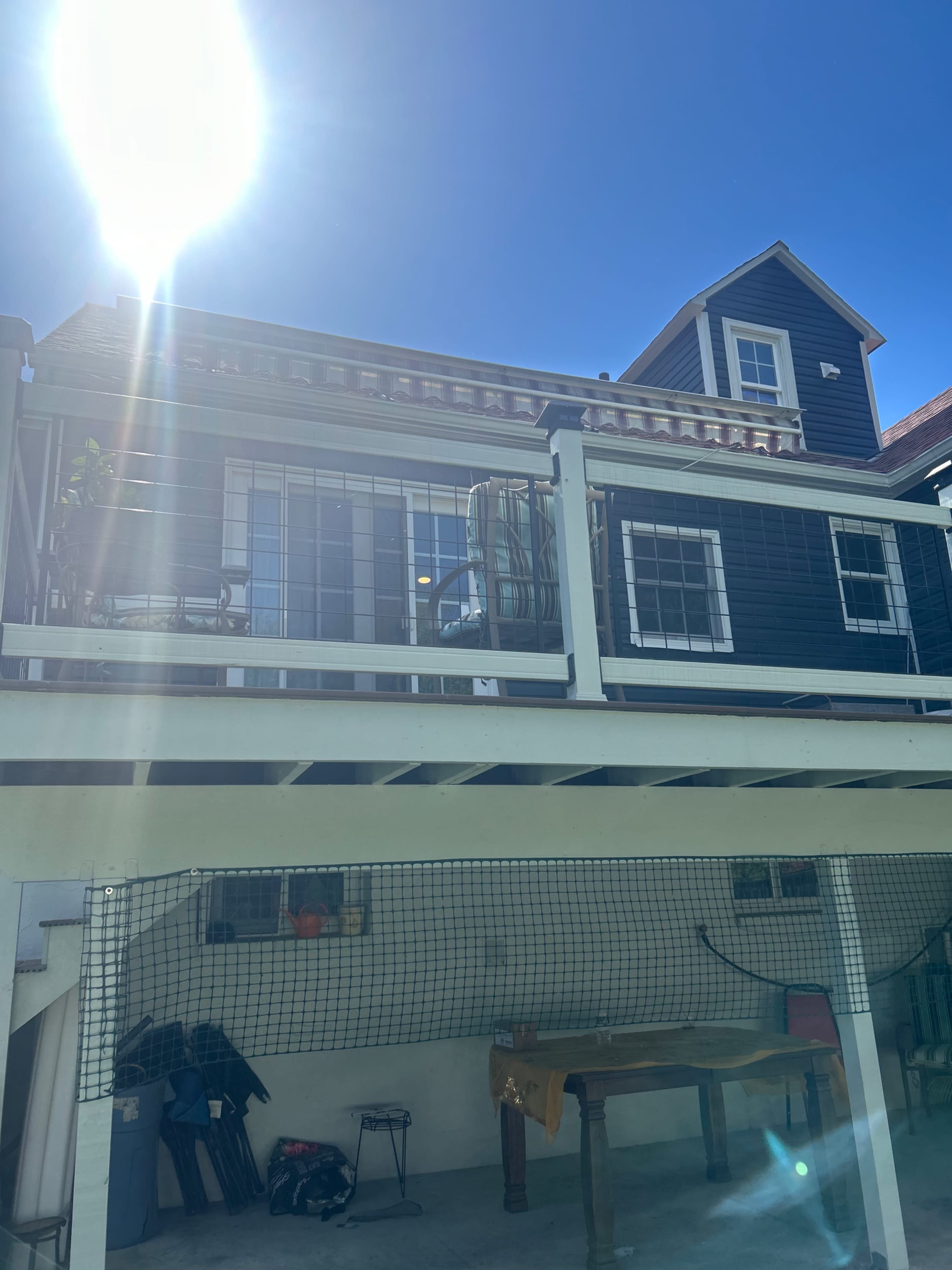 The image shows a two-story house with a balcony on the upper level and a garage area underneath, featuring a netted enclosure.