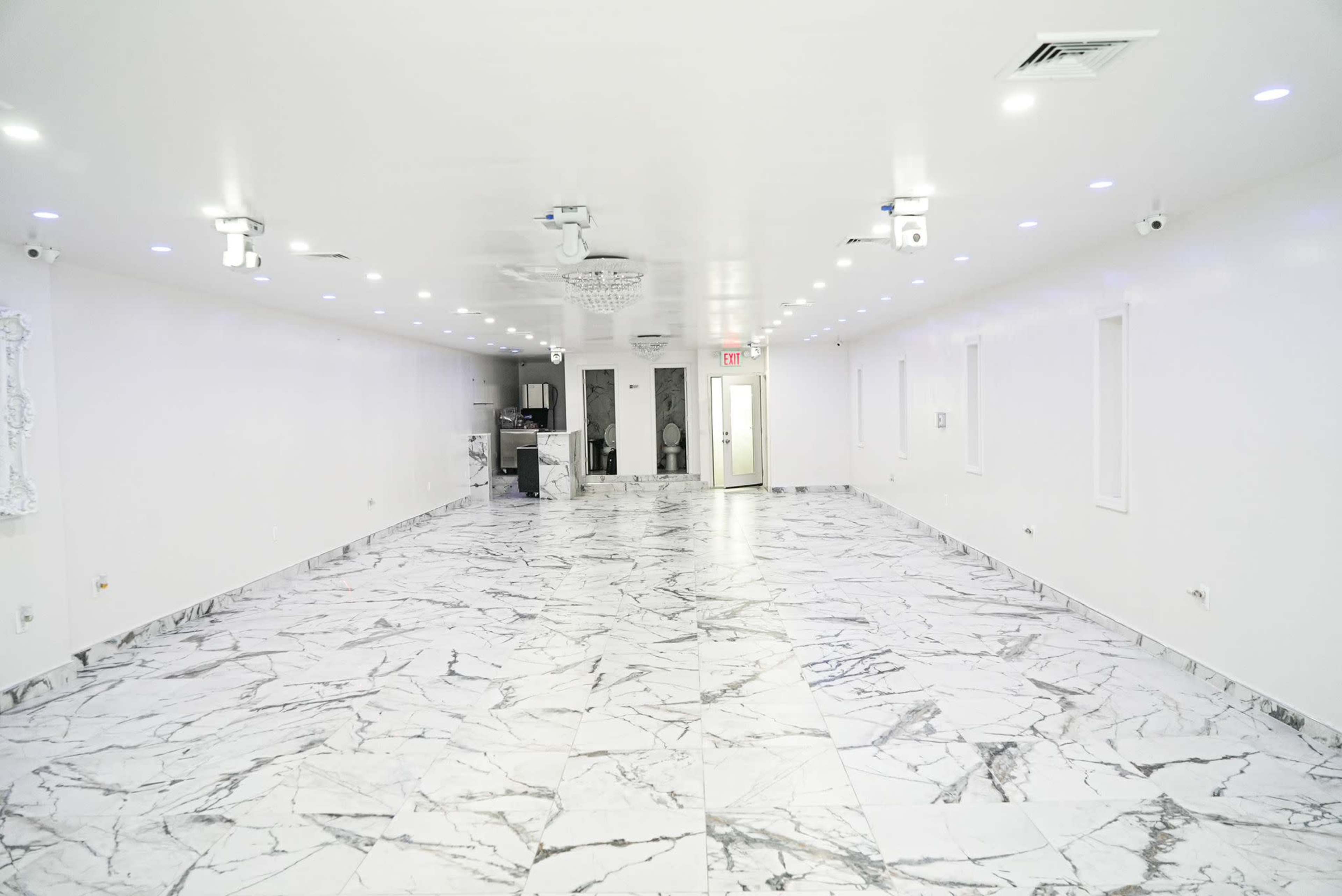 A spacious room with white walls and a marble-patterned floor, illuminated by overhead lights.