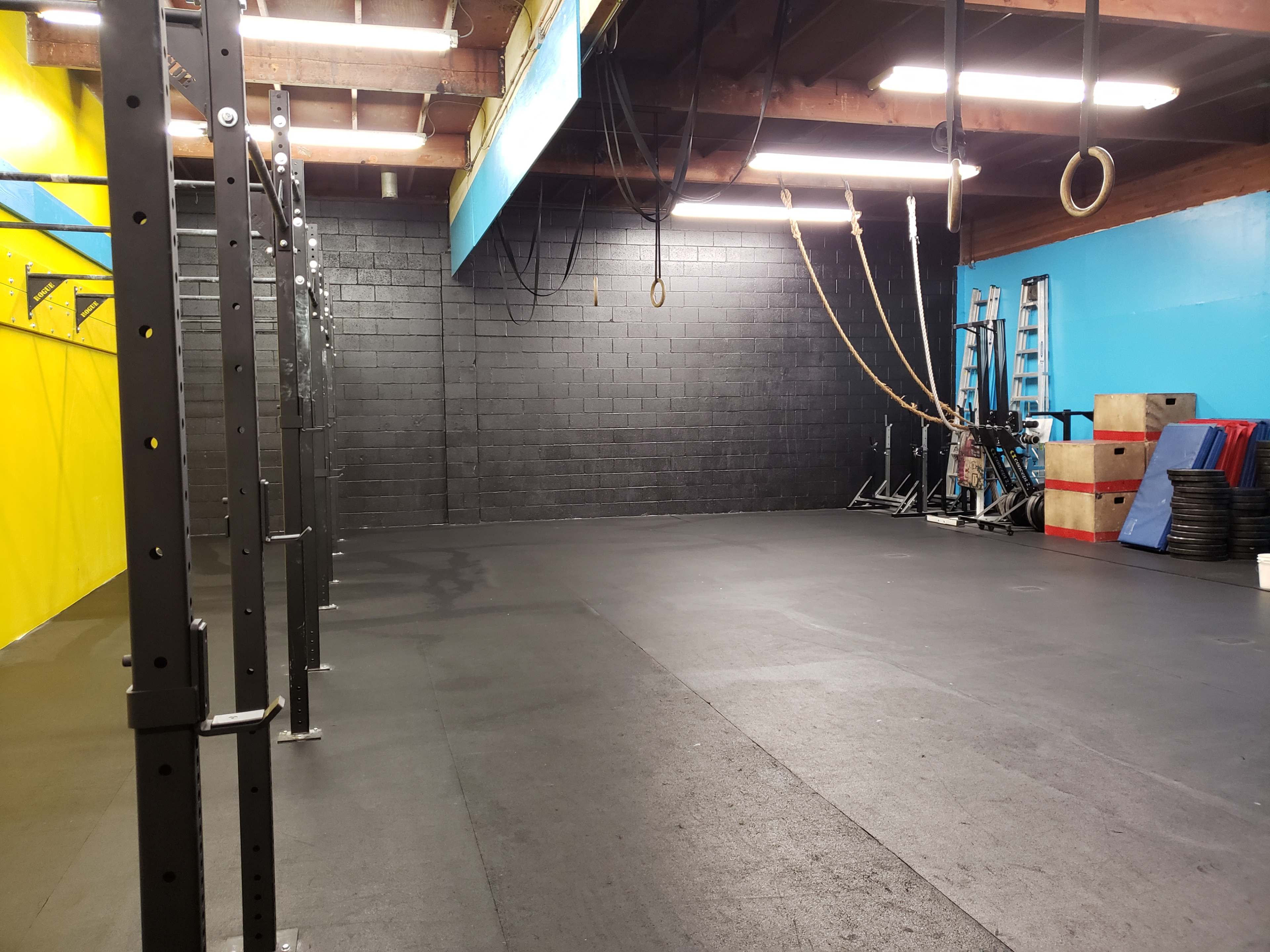 A spacious gym with black rubber flooring, colorful walls, and various fitness equipment arranged on one side.