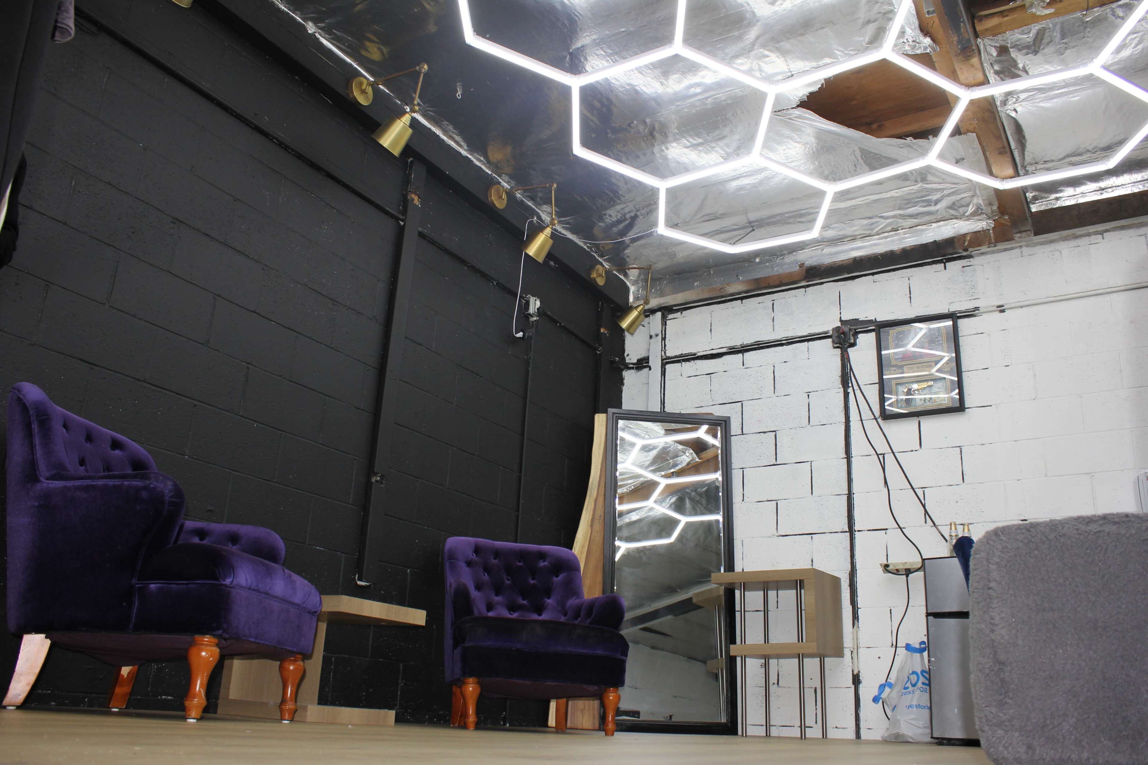 A modern interior space with two purple velvet chairs, a large mirror, and a hexagonal-patterned ceiling light.