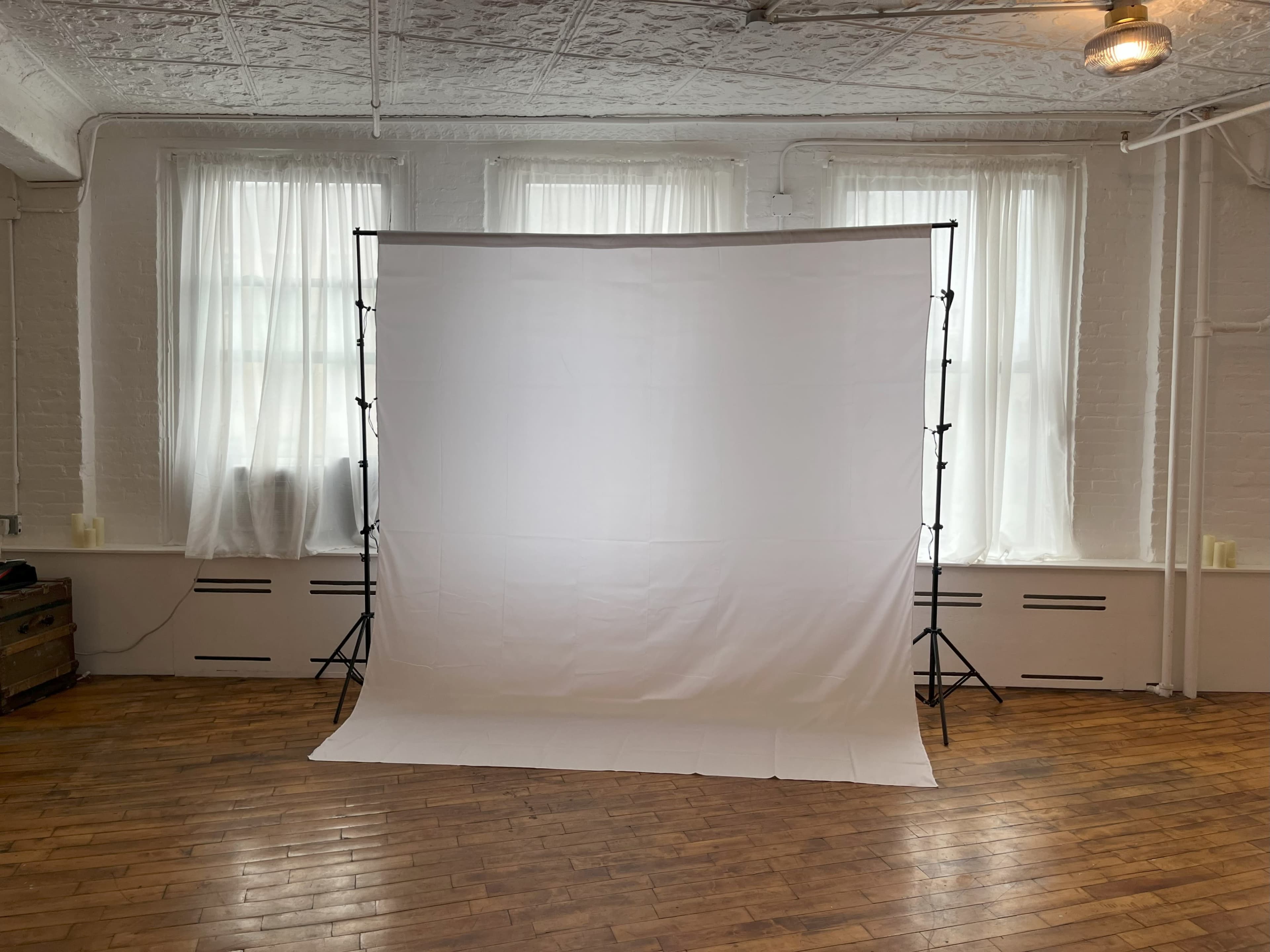 The image shows a white backdrop set up in a brightly lit room with large windows and wooden flooring.