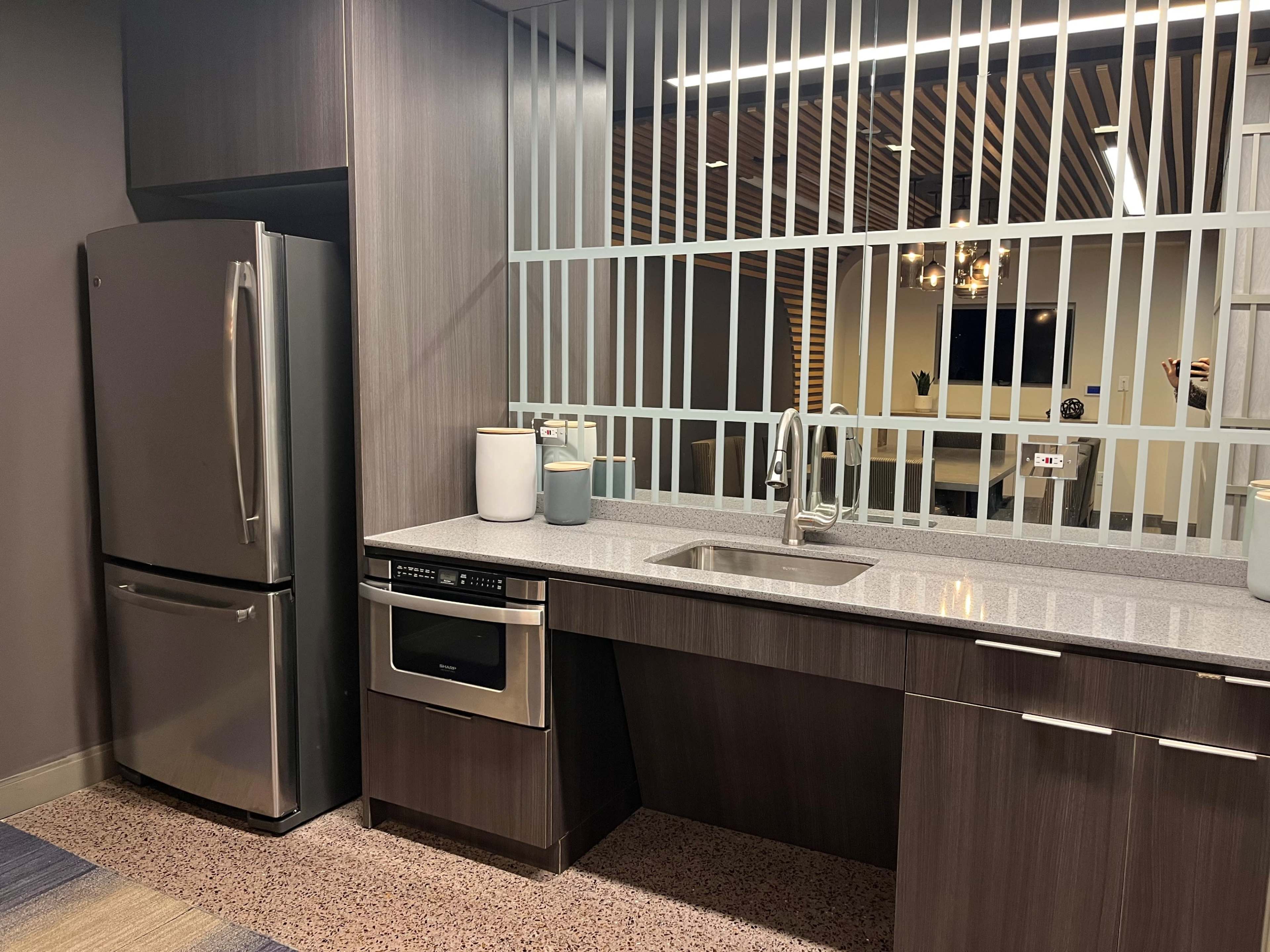 The image shows a modern kitchen with stainless steel appliances, including a refrigerator and an oven, set against a backdrop of wood paneling and a decorative partition.