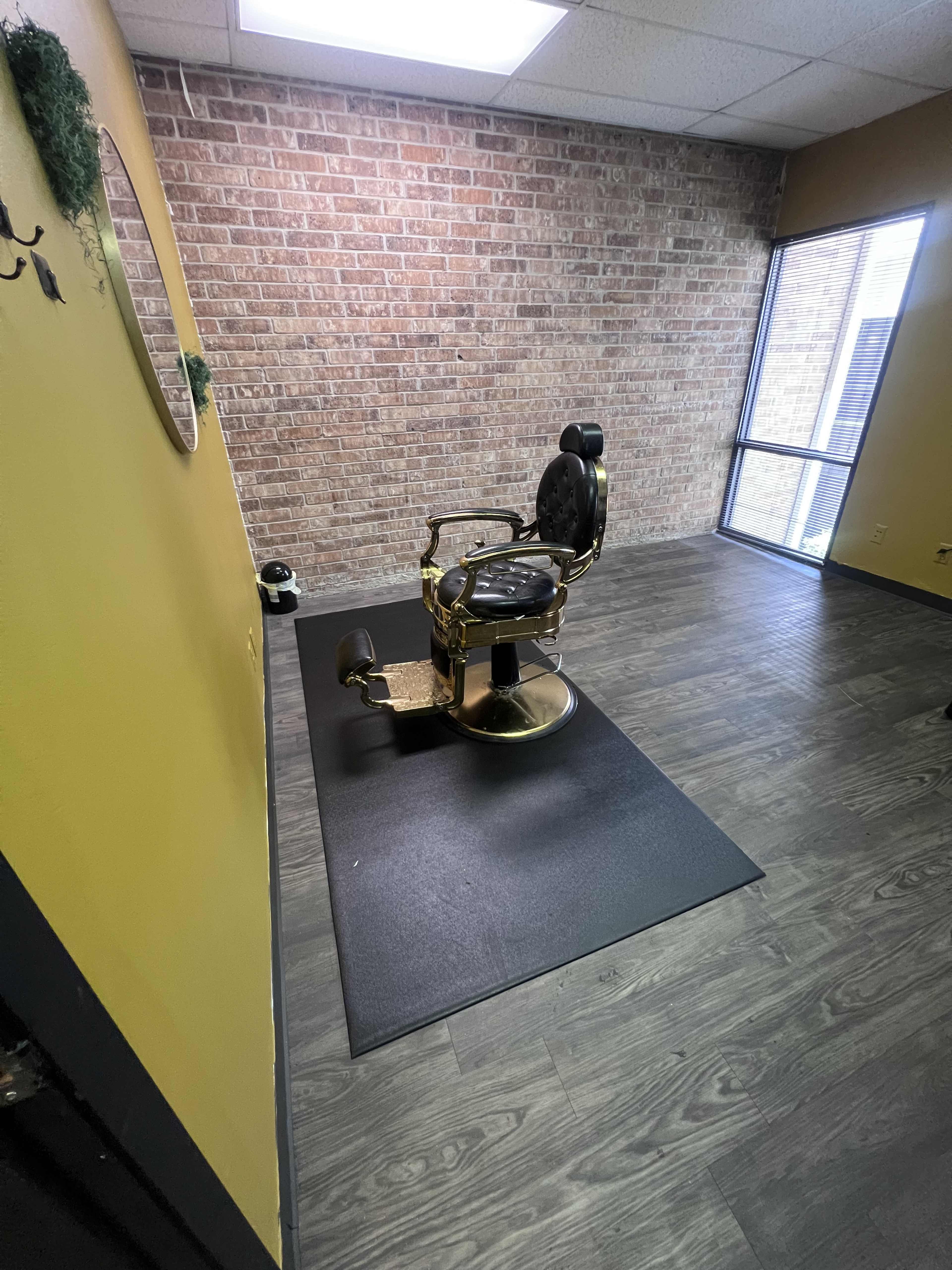 A vintage barber chair positioned on a black mat in a room with brick walls and large windows.