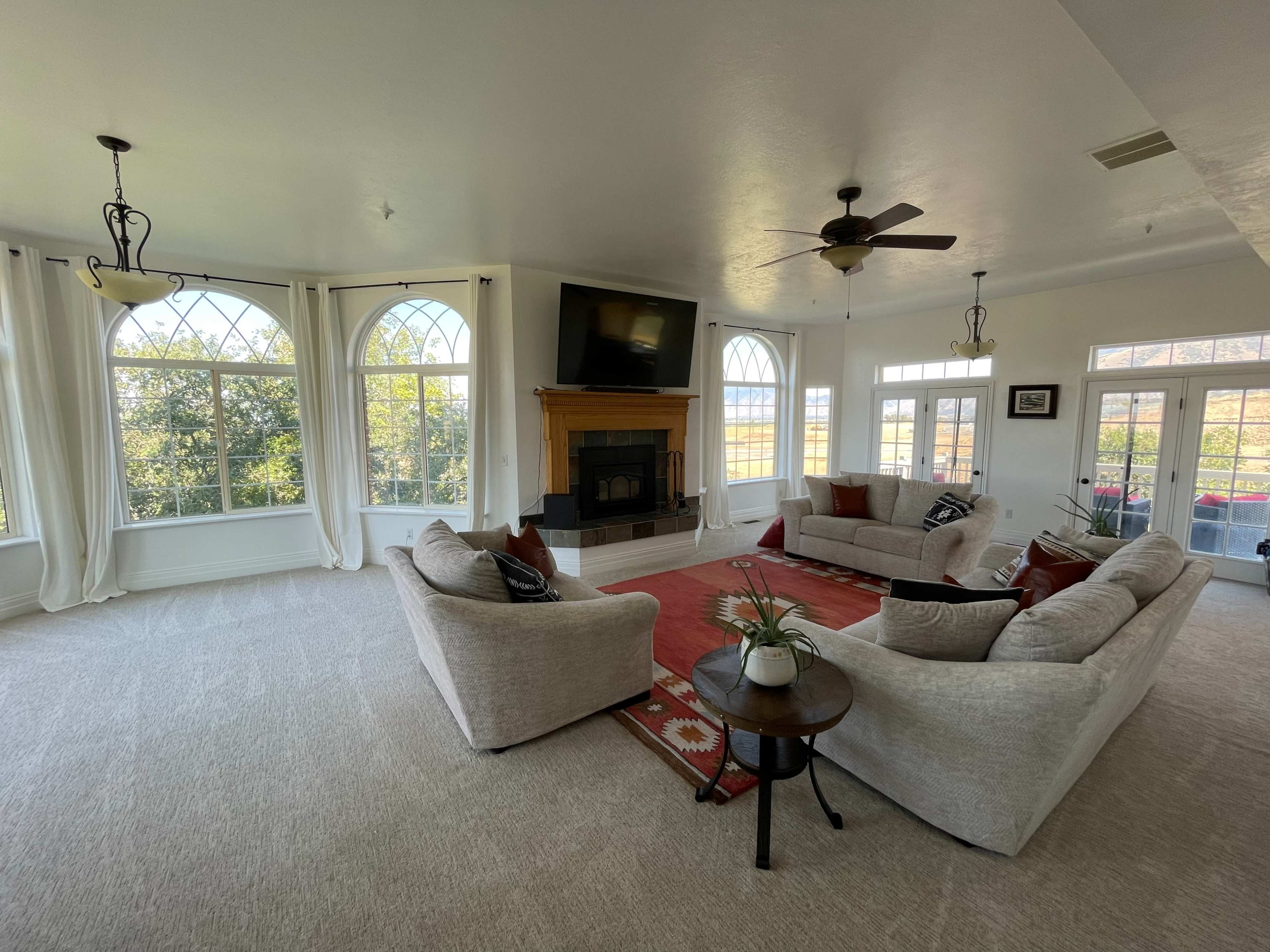 A spacious living room featuring two large sofas, a fireplace with a television above it, and large windows letting in natural light.