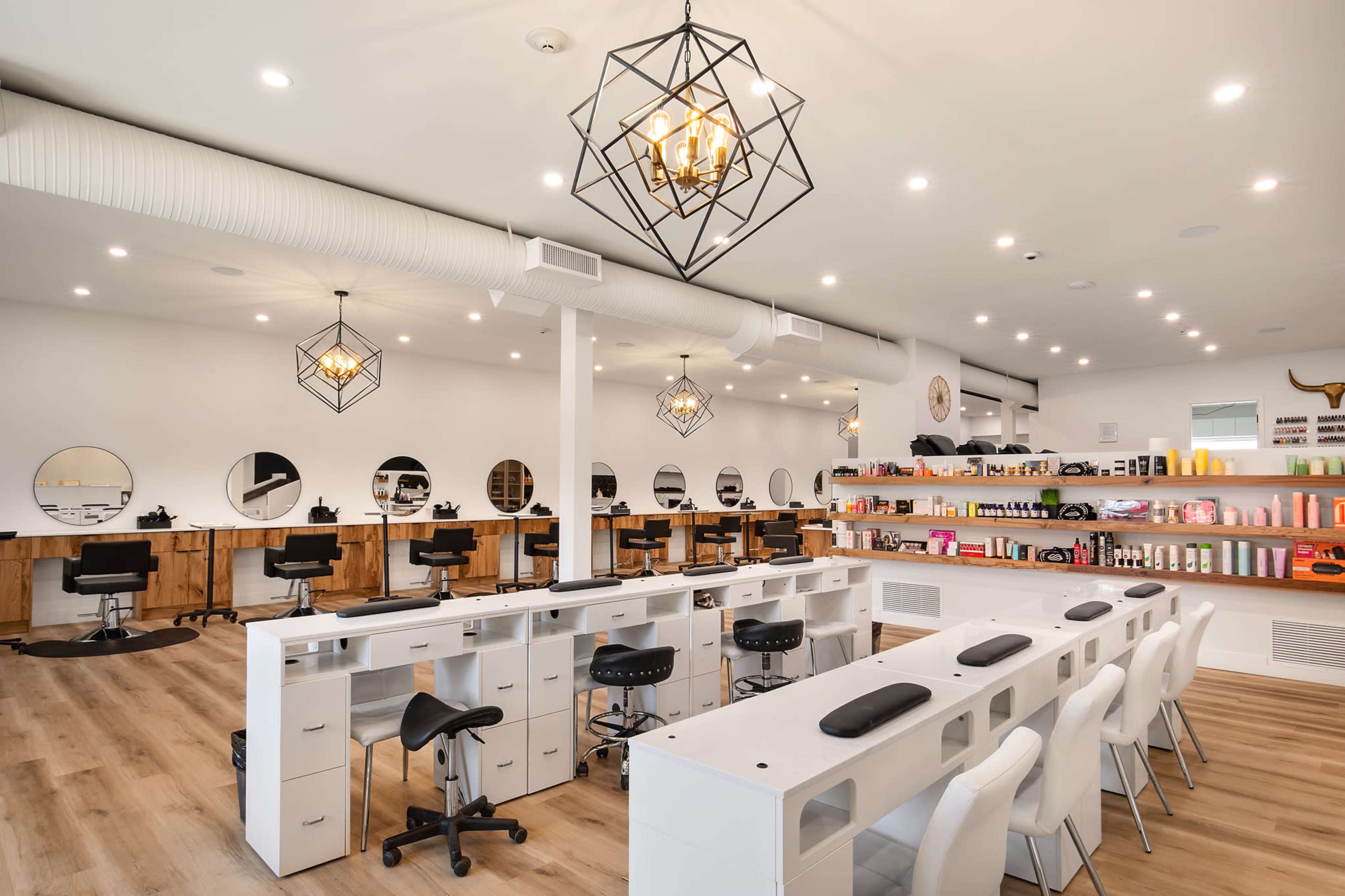 The image shows a modern salon interior featuring styling chairs at individual stations, a row of circular mirrors, and neatly arranged shelves with various hair and beauty products.