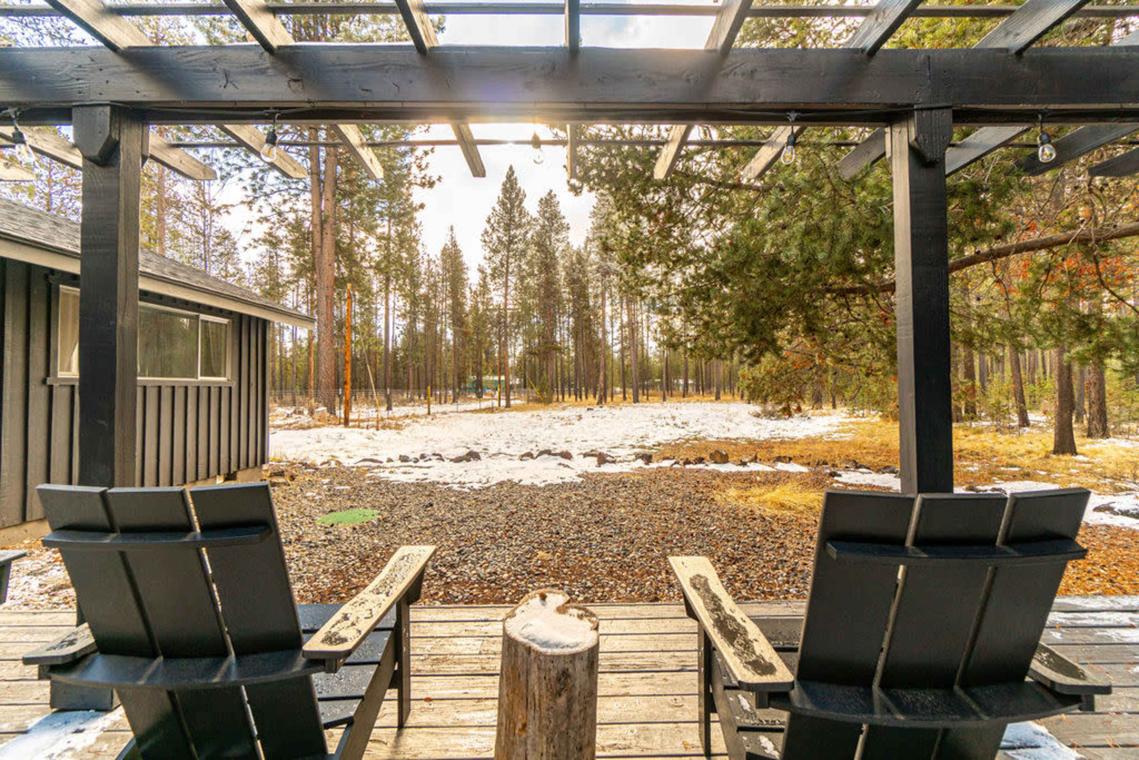 Two adirondack chairs sit on a wooden deck overlooking a snowy and wooded landscape.