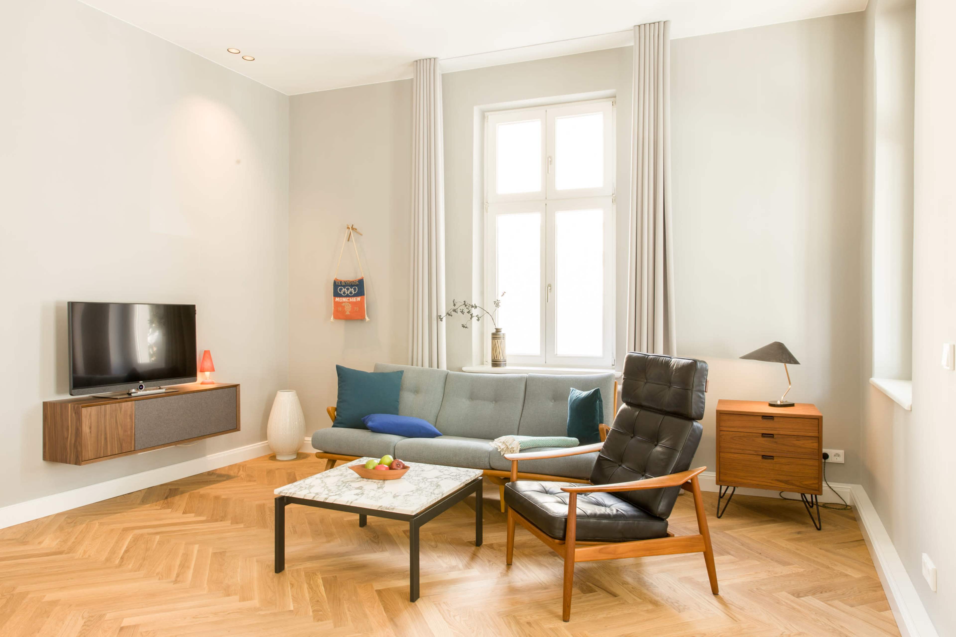 A modern living room features a grey sofa, a black lounge chair, a marble coffee table, and a television mounted on the wall.