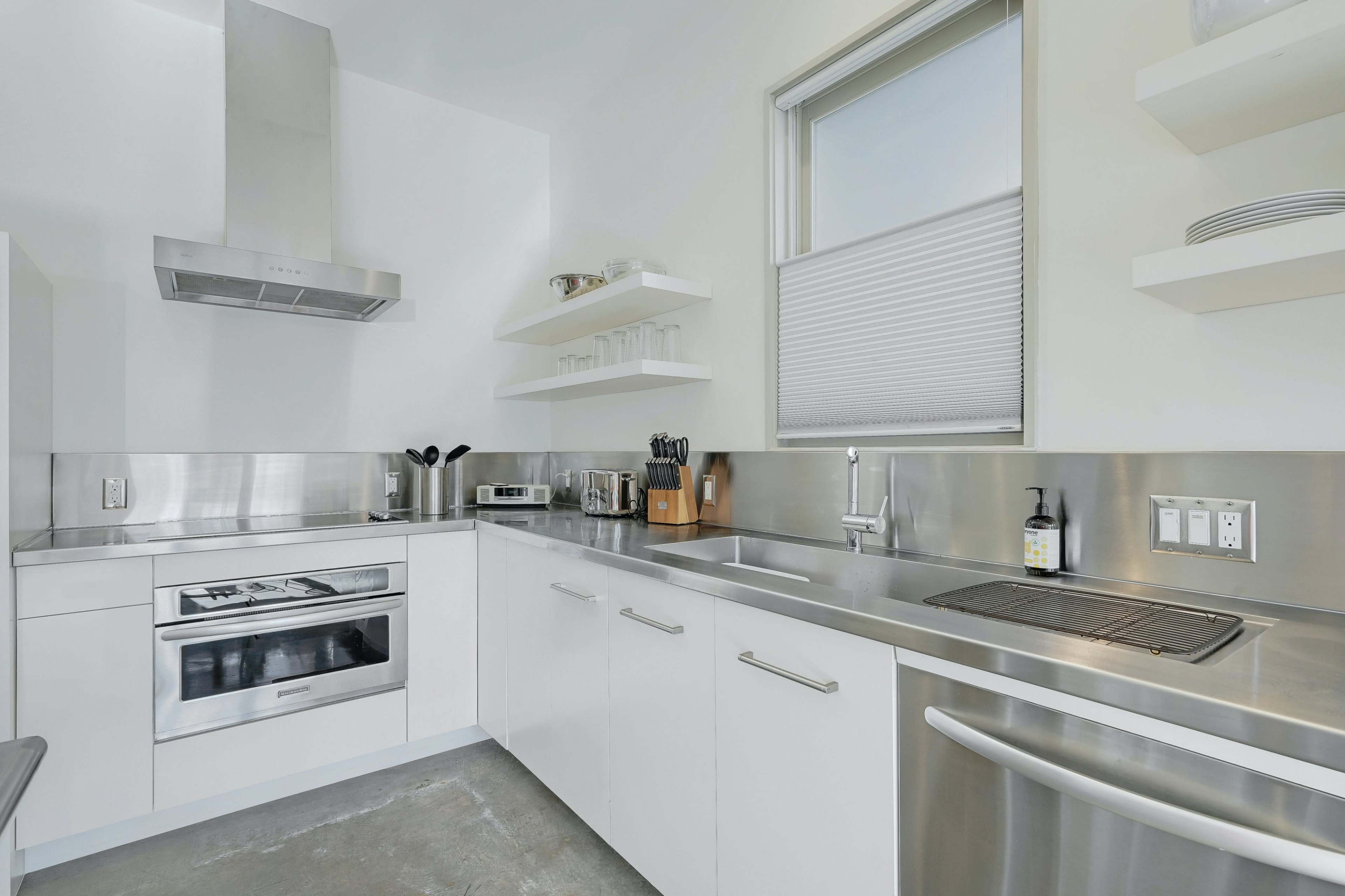 The kitchen features stainless steel appliances, white cabinetry, and a minimalist design with open shelves.