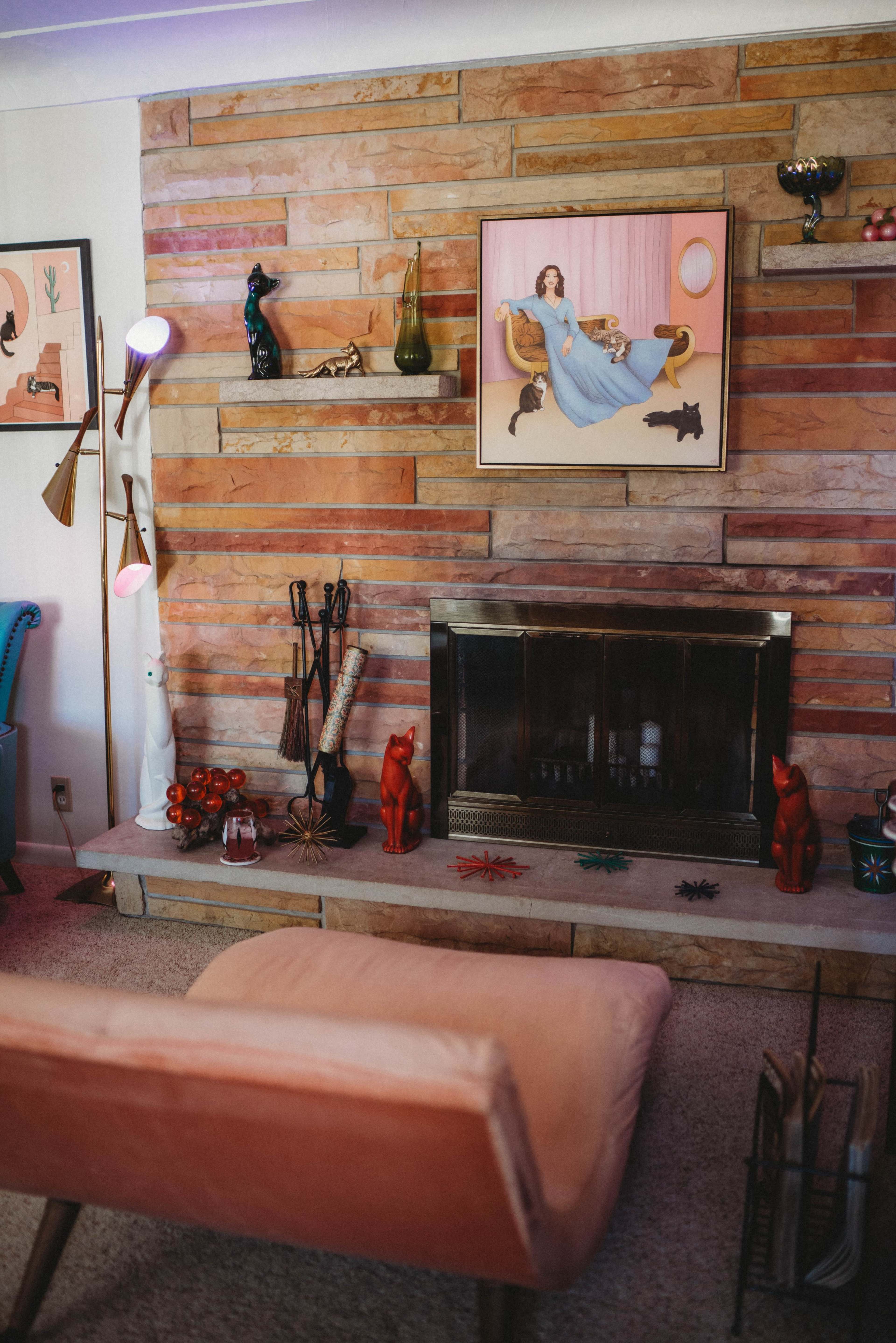 The image shows a living room featuring a stone wall, a fireplace with decorative items, and a pink lounge chair.