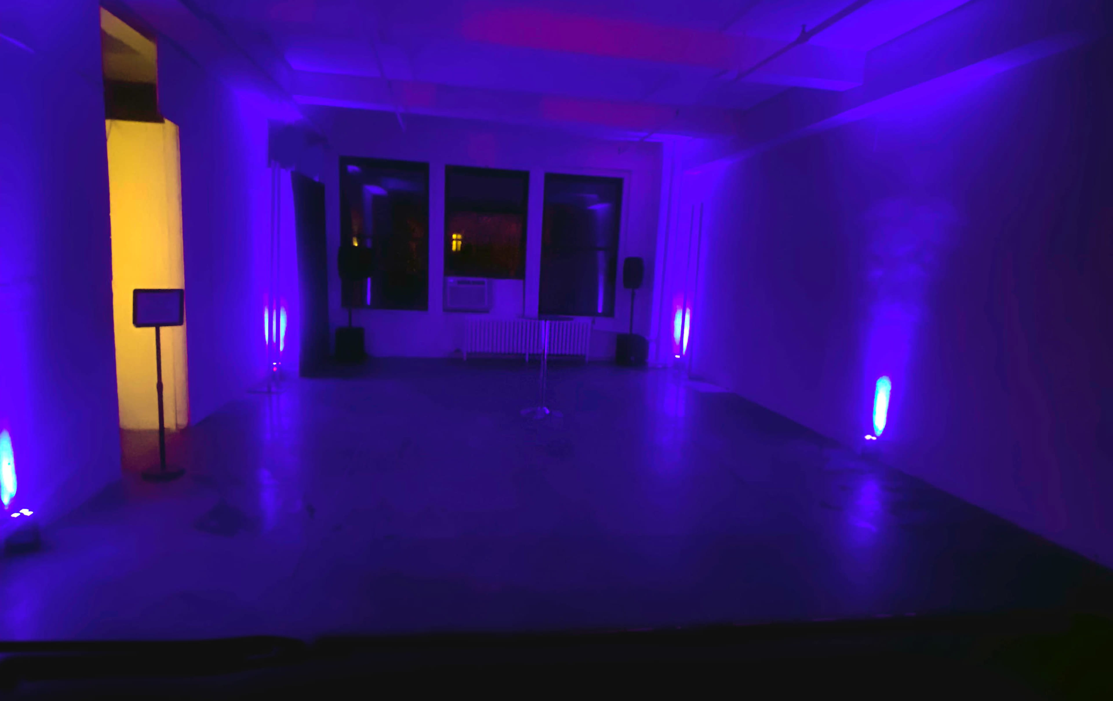 The image shows an empty room with purple ambient lighting, featuring two floor lights and a microphone stand in the center.