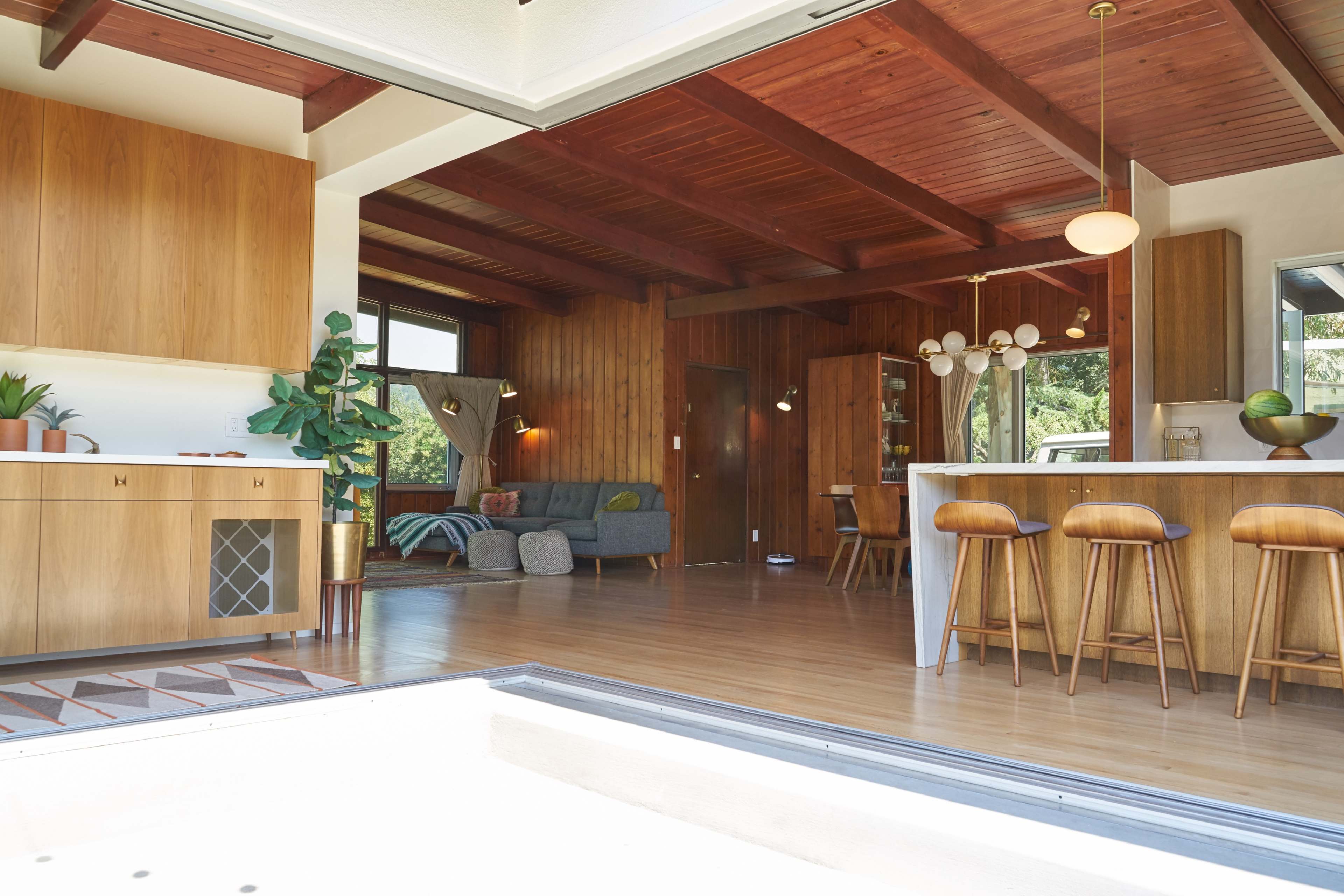 A modern open-concept living space that features a kitchen with wooden cabinetry, a dining area with bar stools, and a cozy seating area with a sofa.