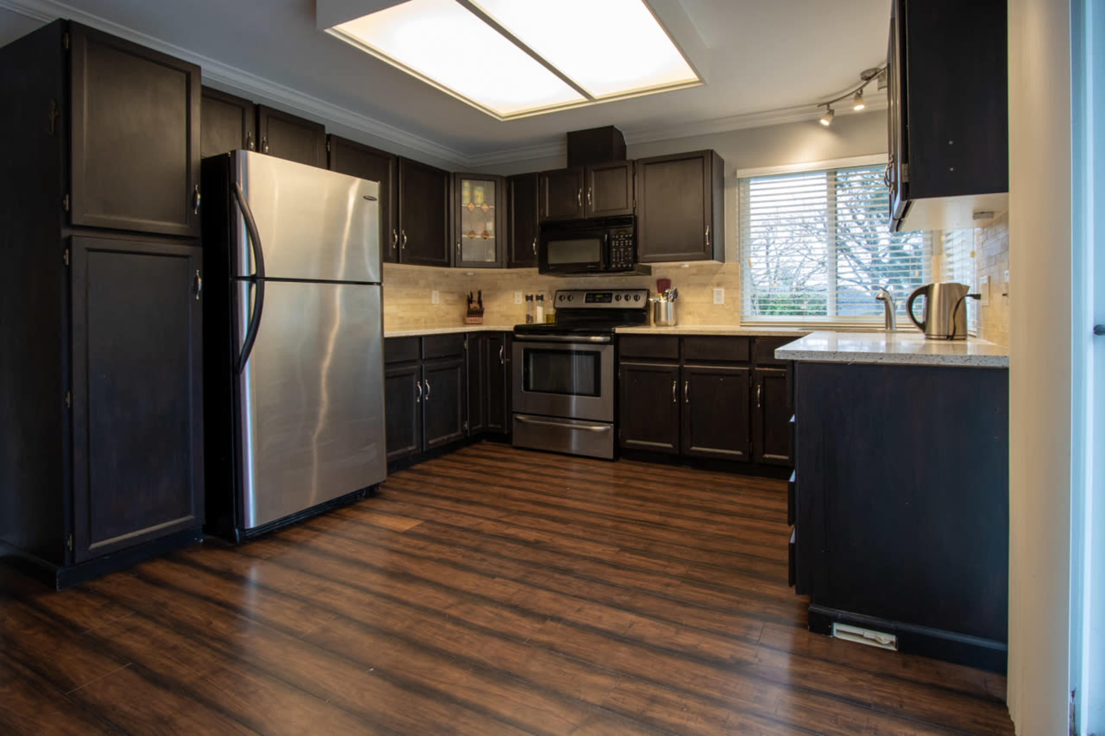 The kitchen features dark cabinetry, a stainless steel refrigerator, an oven, and a window with blinds.