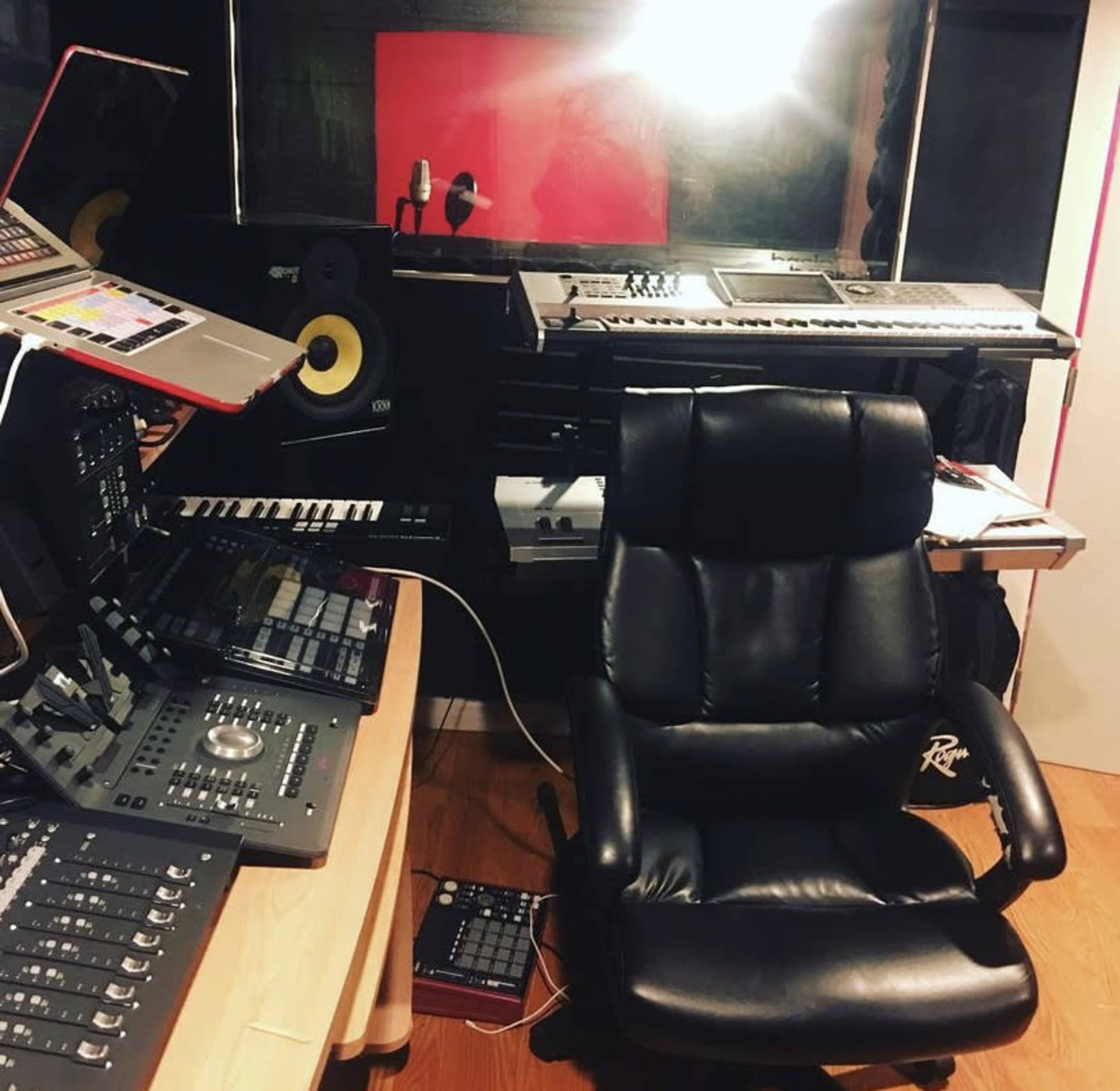 A music studio with various electronic instruments, a mixing console, and a black leather chair.