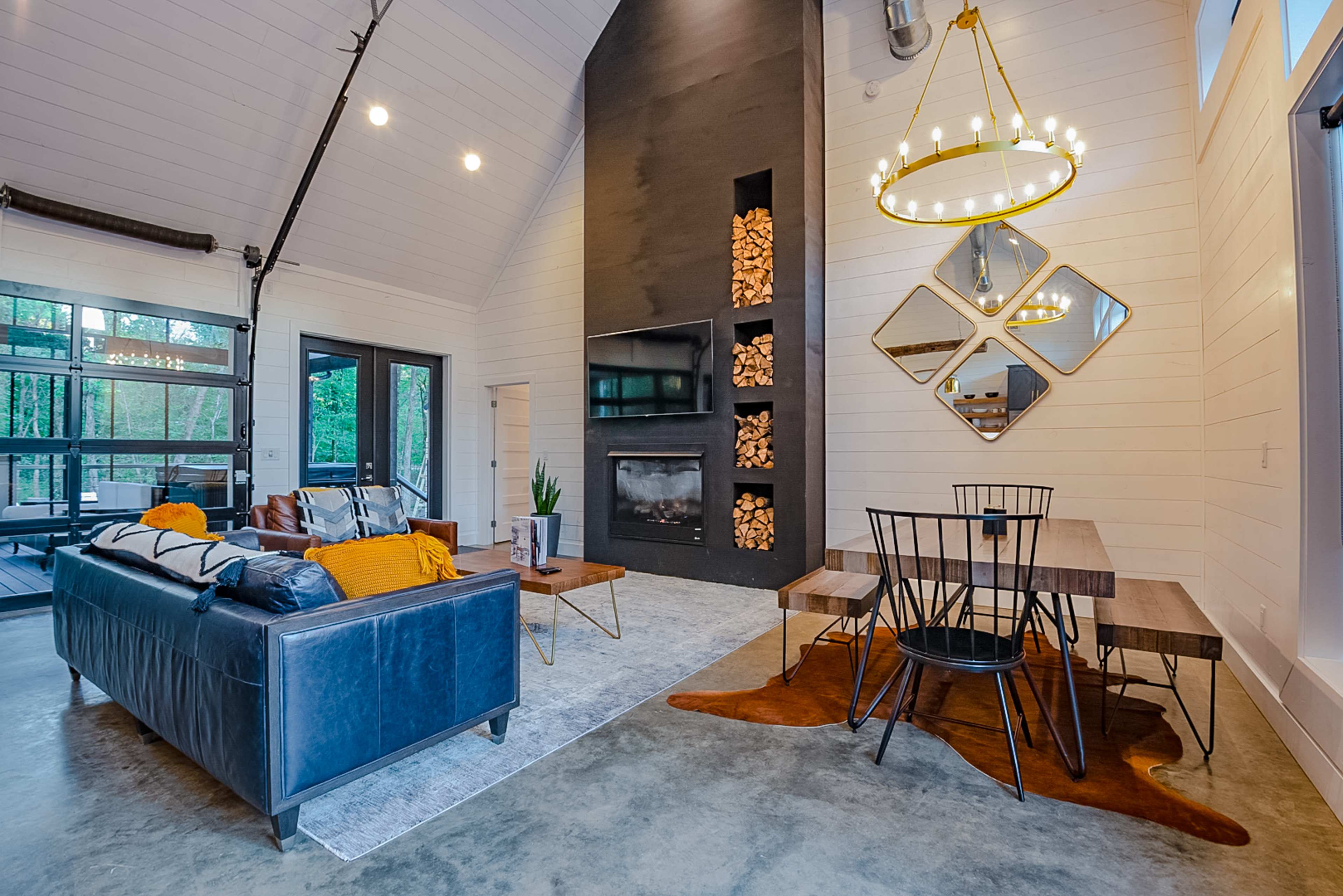 A modern living room with a black feature wall that has a fireplace, a seating area with a dark couch and coffee table, and a dining table with chairs on a concrete floor.
