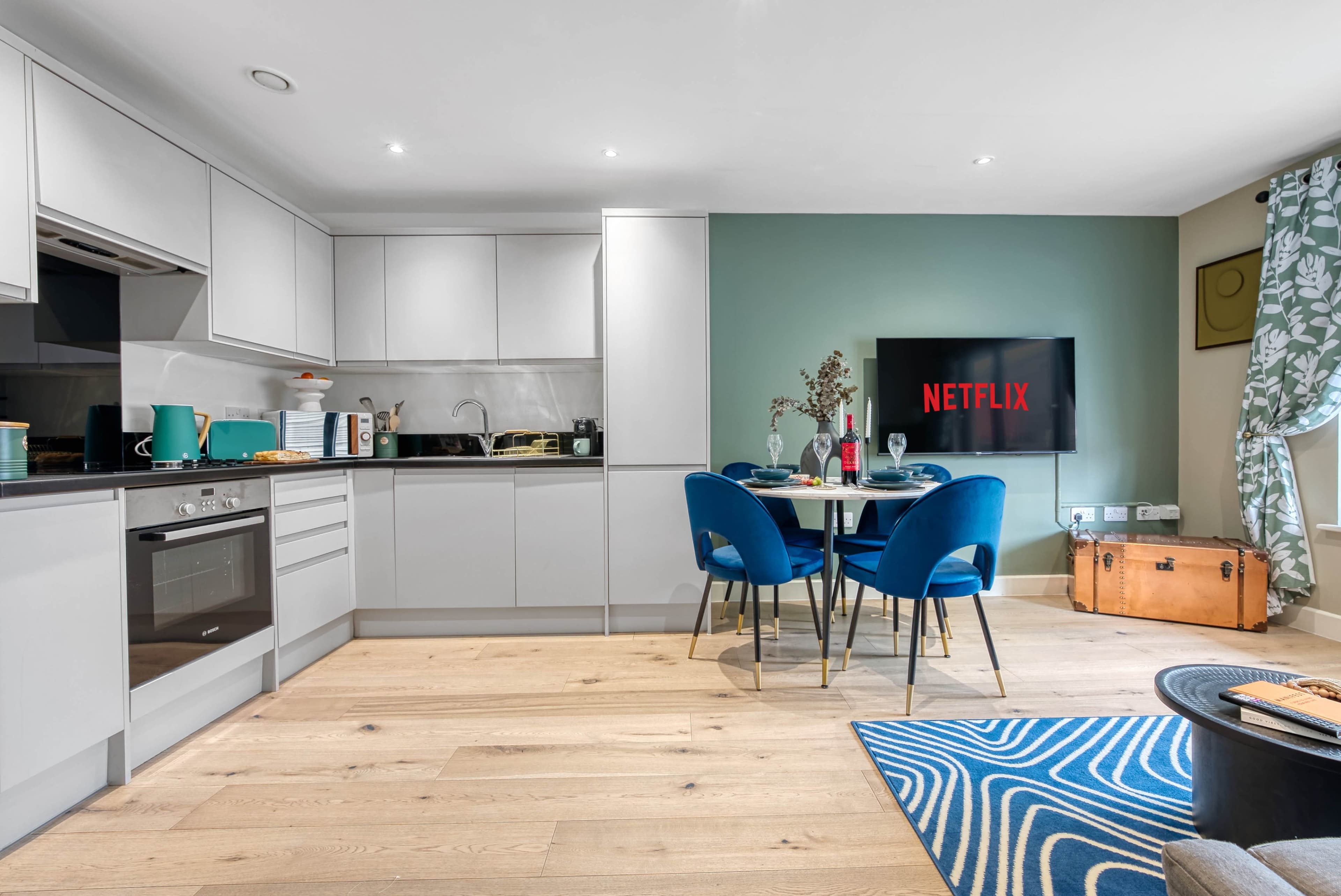 The image shows a modern kitchen and dining area with a Netflix logo displayed on a wall-mounted TV.