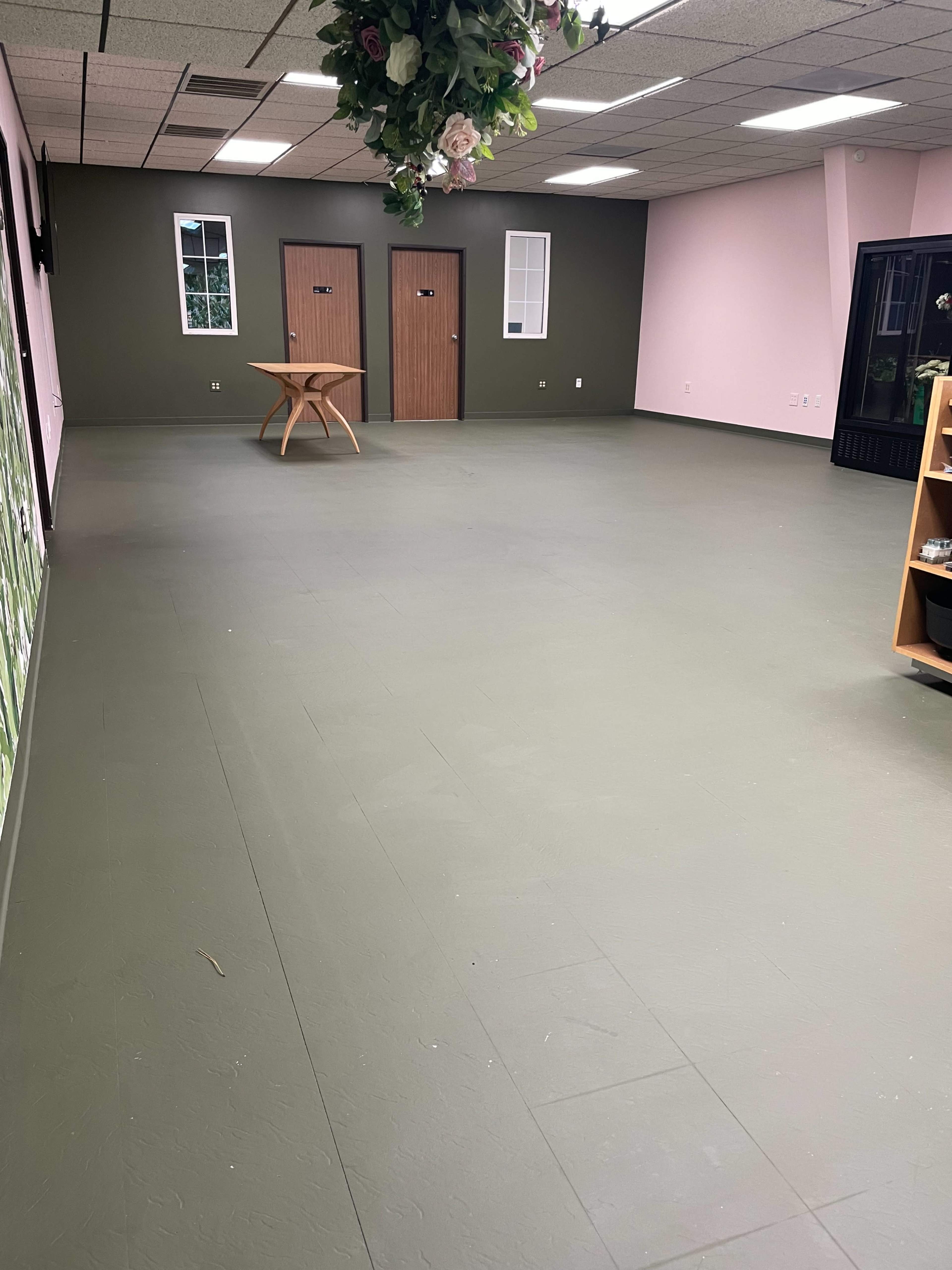 An empty room with green and pink walls, a wooden table in the center, and two doors at the far end.