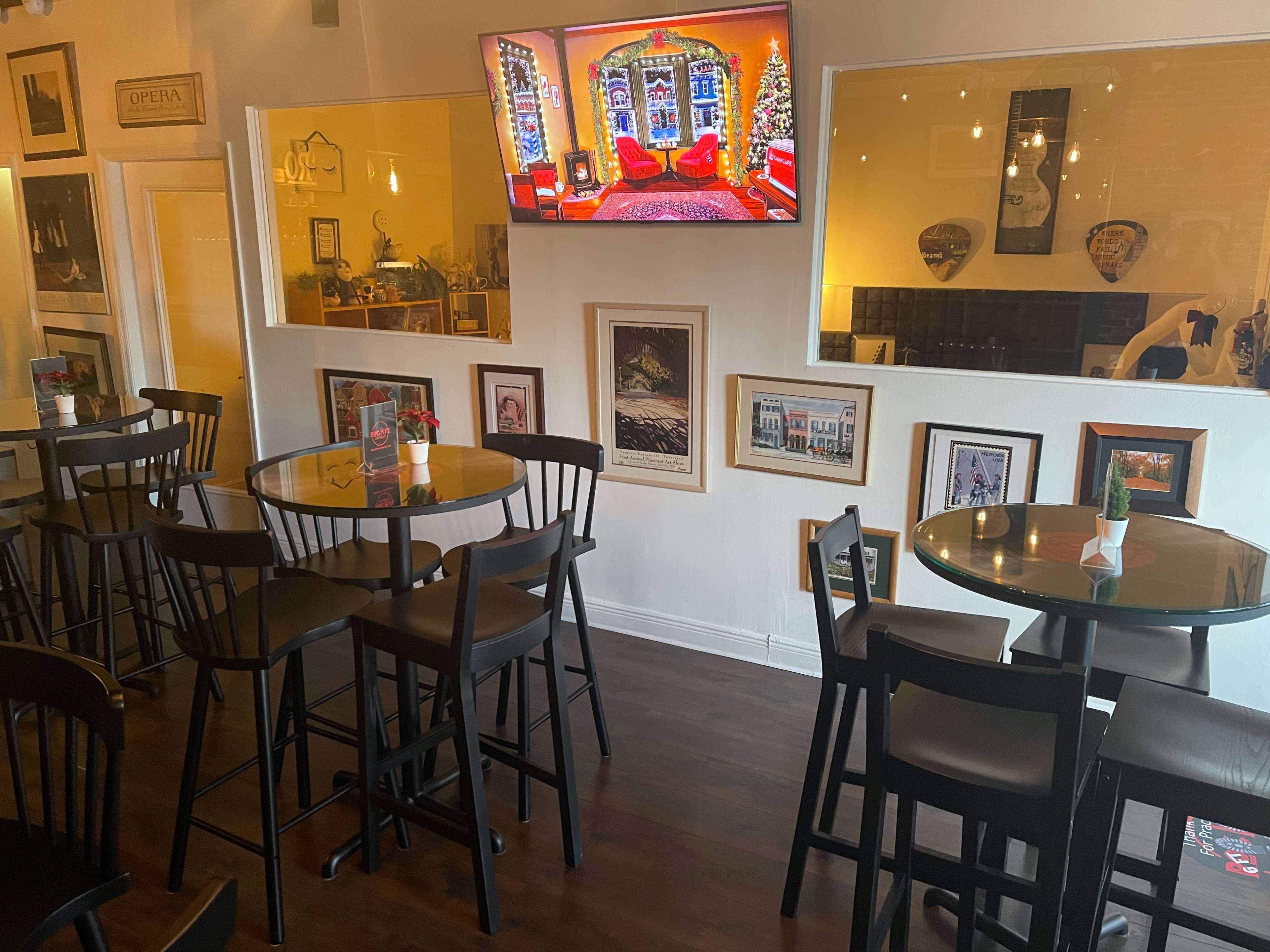 The scene shows a cozy restaurant interior with high tables and chairs, featuring framed photographs on the walls and a television displaying a festive scene.
