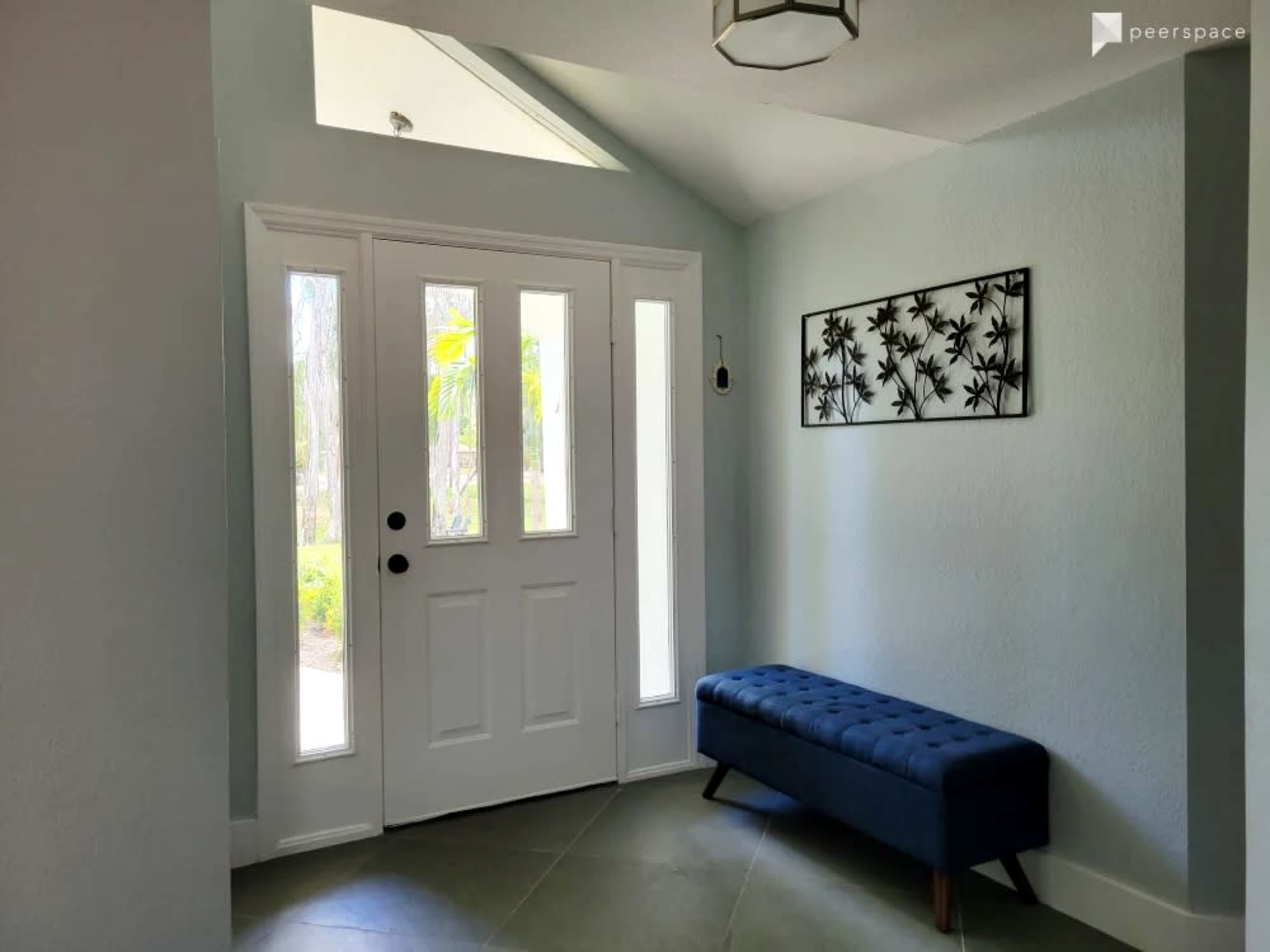 A bright entryway featuring a white door with glass paneling, light blue walls, and a dark blue upholstered bench against the wall.