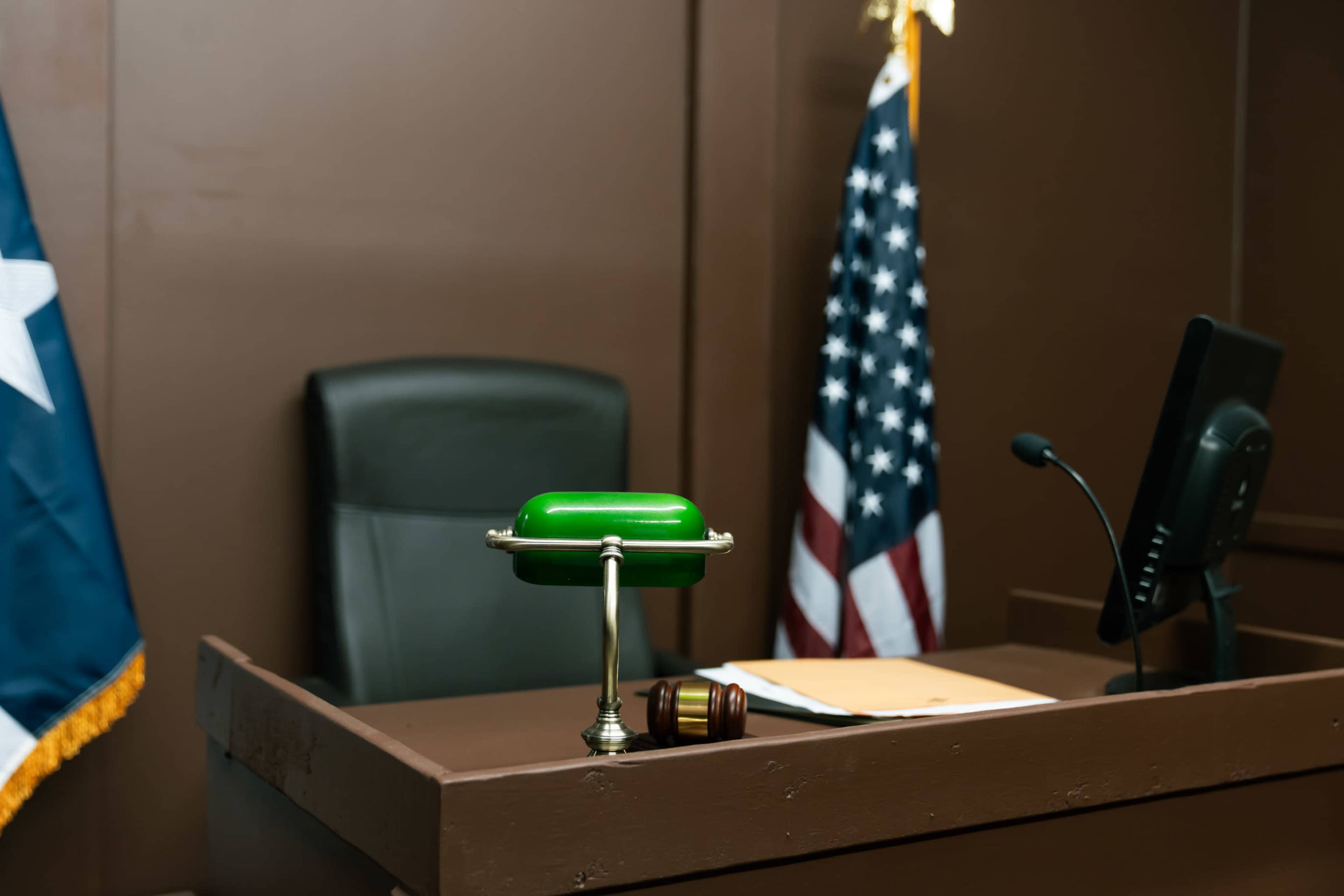 A courtroom scene shows a judge's bench with a green brass lamp, a gavel, and an American flag.