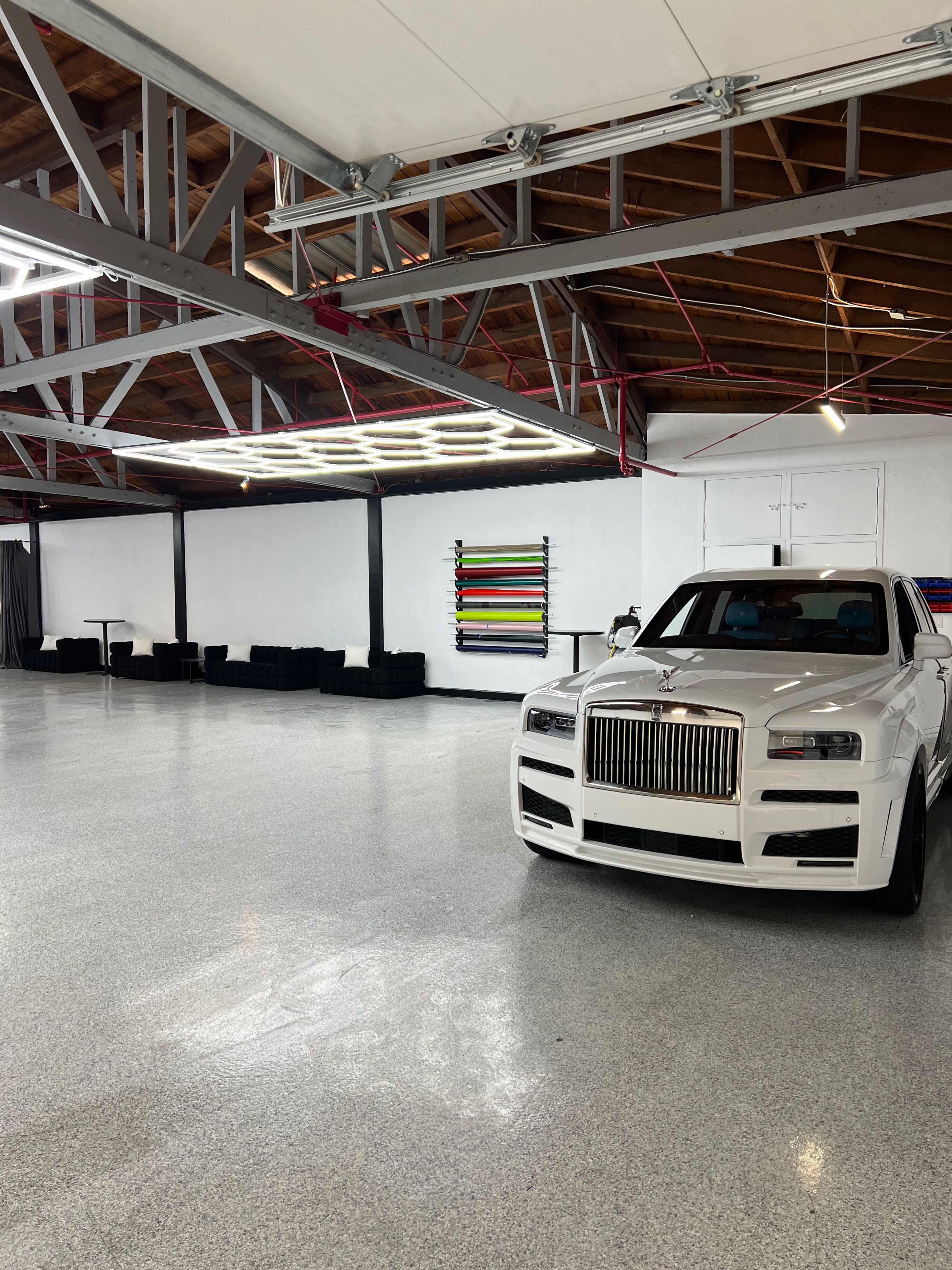 A luxury white car is parked in a spacious, empty garage with white walls and a polished concrete floor.