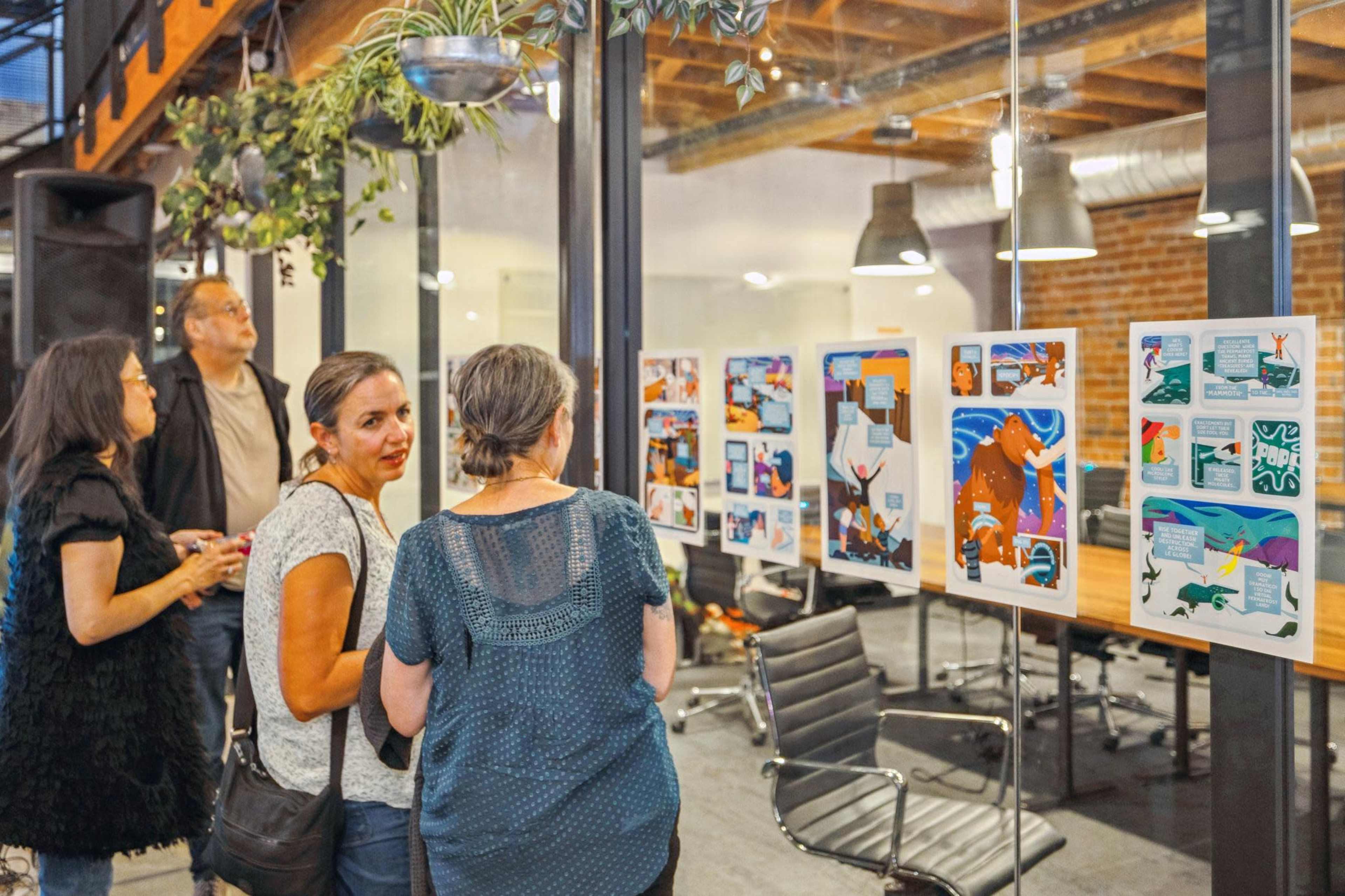 A group of people stands in a modern workspace, examining colorful artwork displayed on panels.