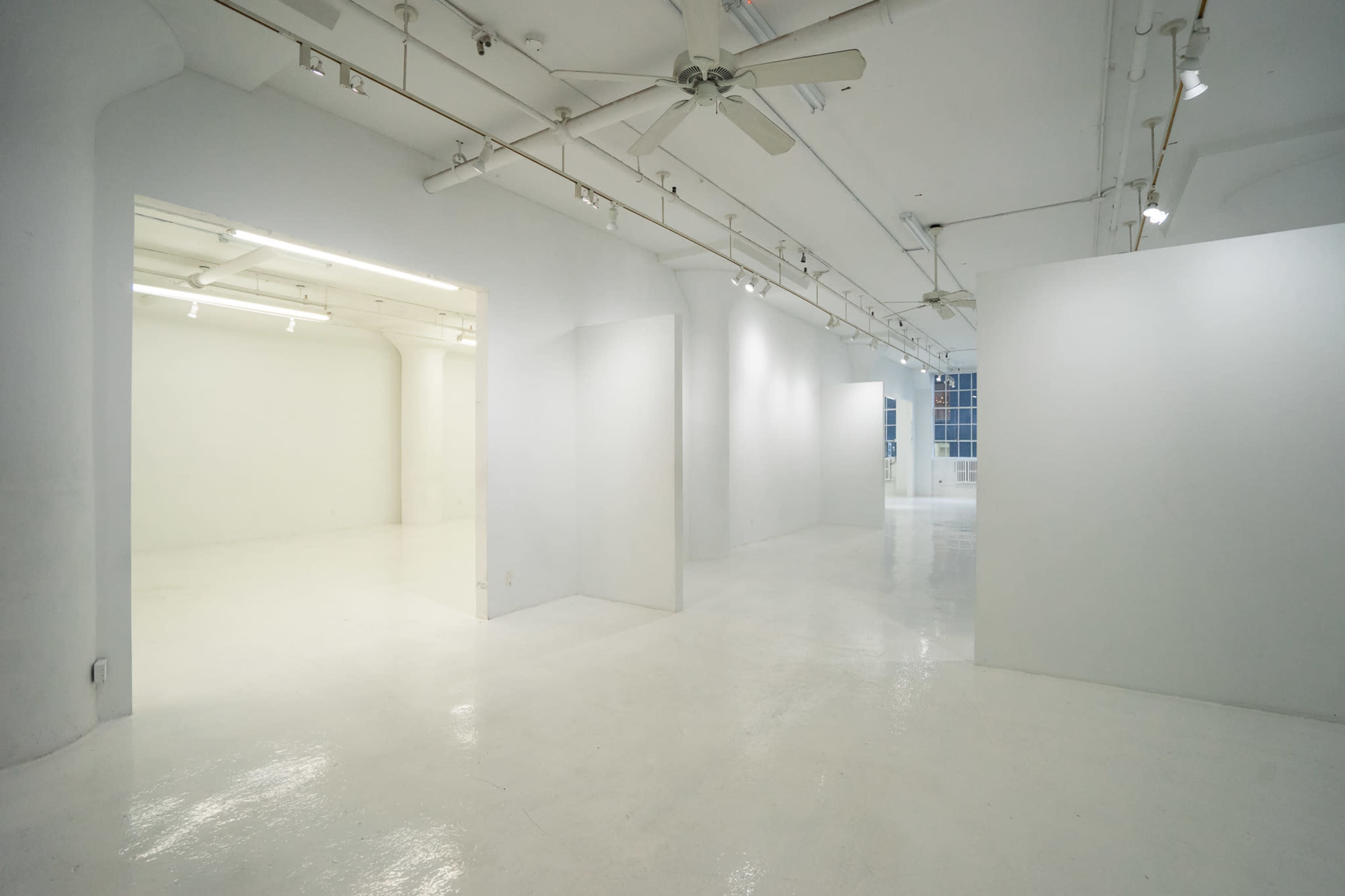 A spacious, minimalist gallery with white walls, a polished floor, and overhead lighting.