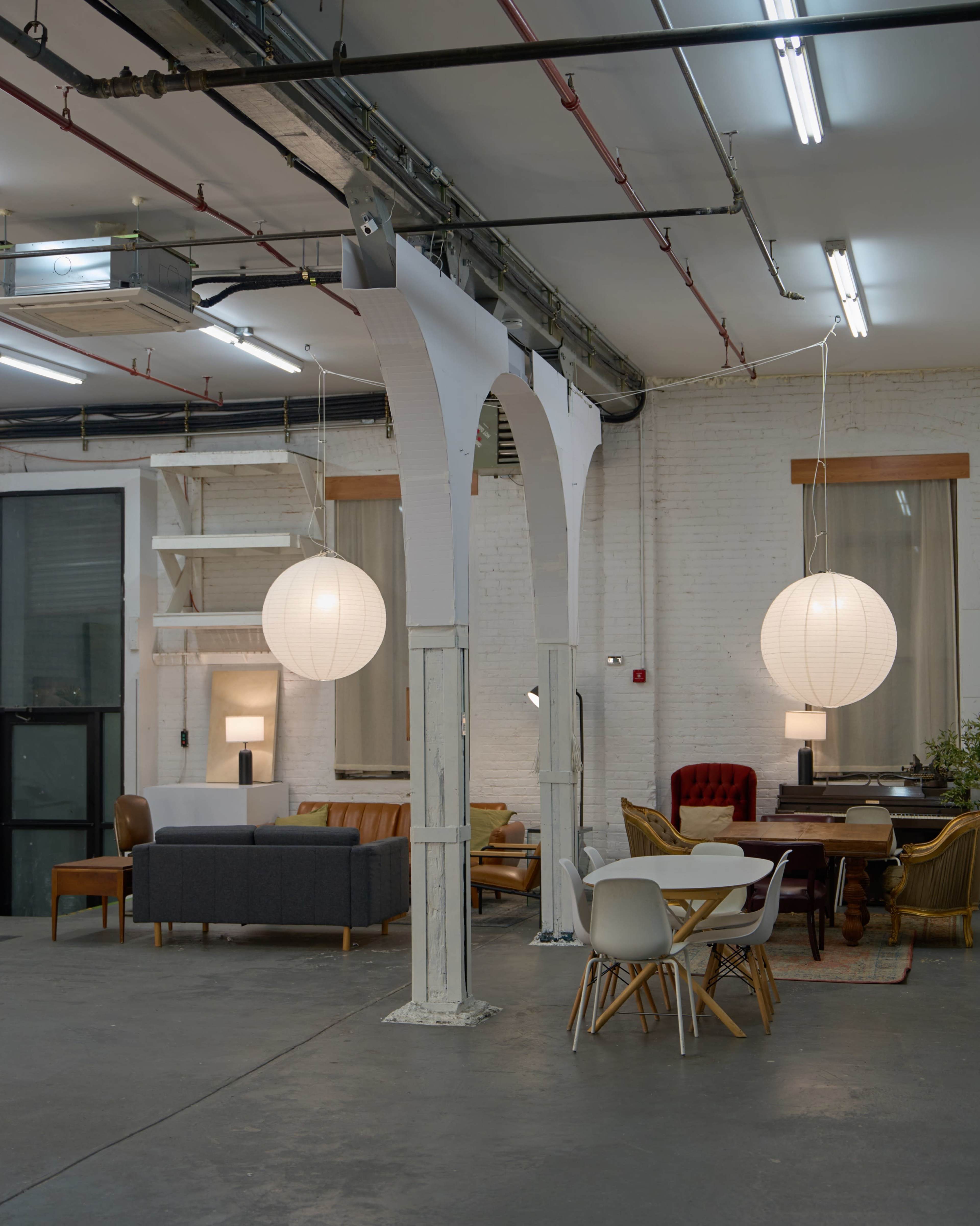 The image shows an industrial-style interior space featuring a mix of seating options, decorative pendant lights, and exposed architectural elements.