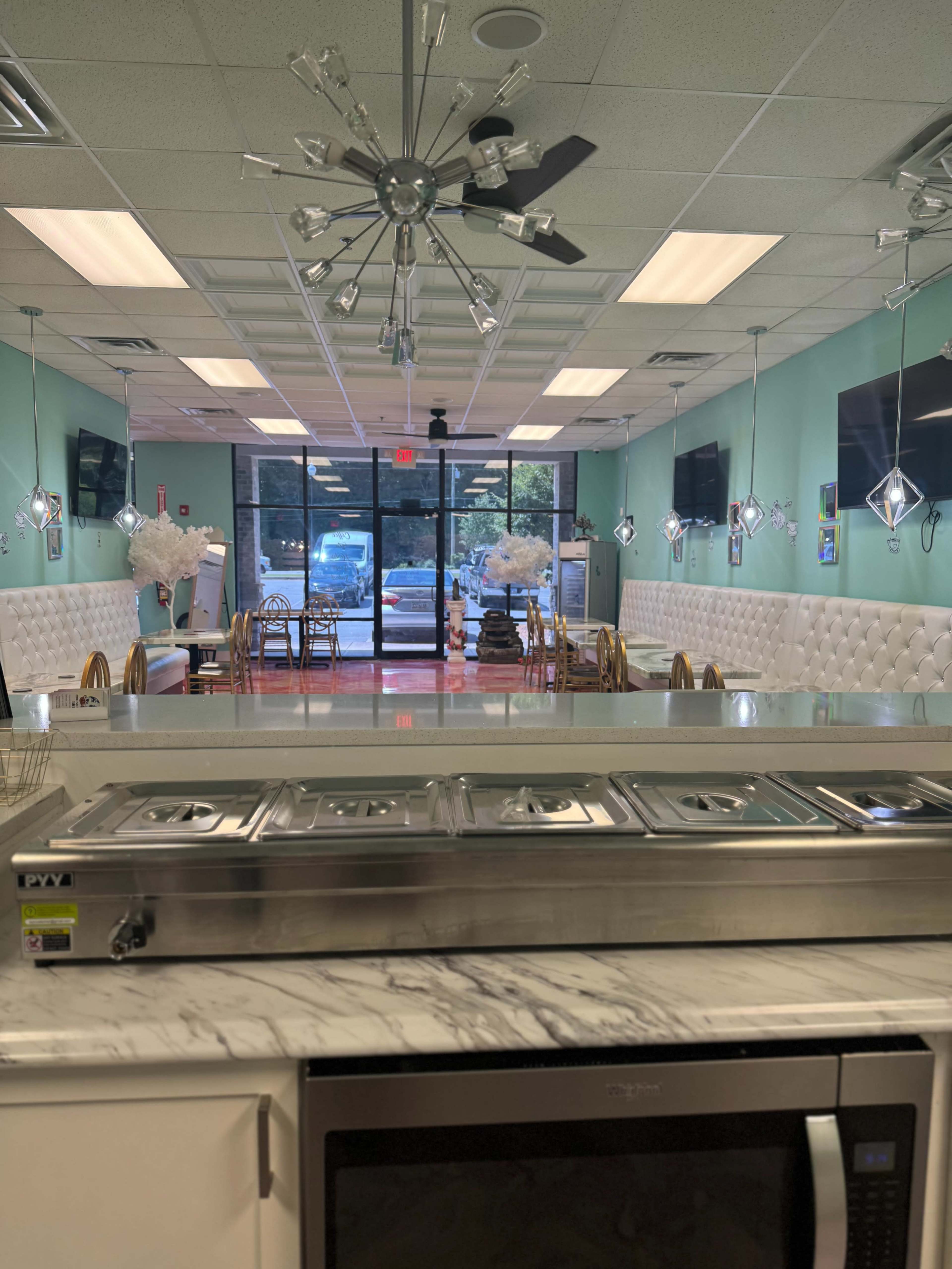 The image shows a spacious, brightly lit restaurant interior with a marble countertop in the foreground, tables and chairs arranged in the dining area, and large windows at the back.