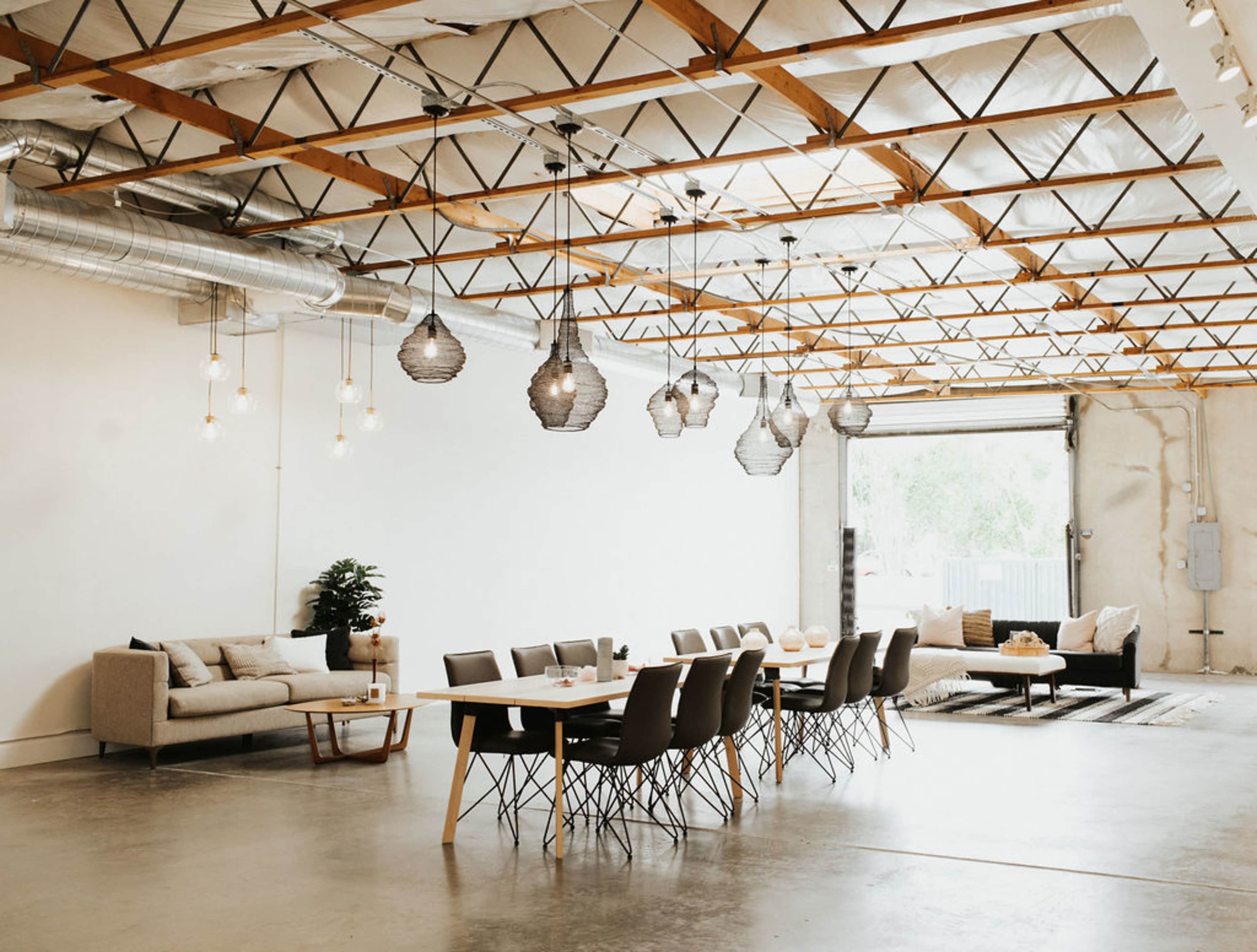 A spacious interior with a dining table surrounded by chairs, a sofa, and hanging light fixtures under a vaulted ceiling.