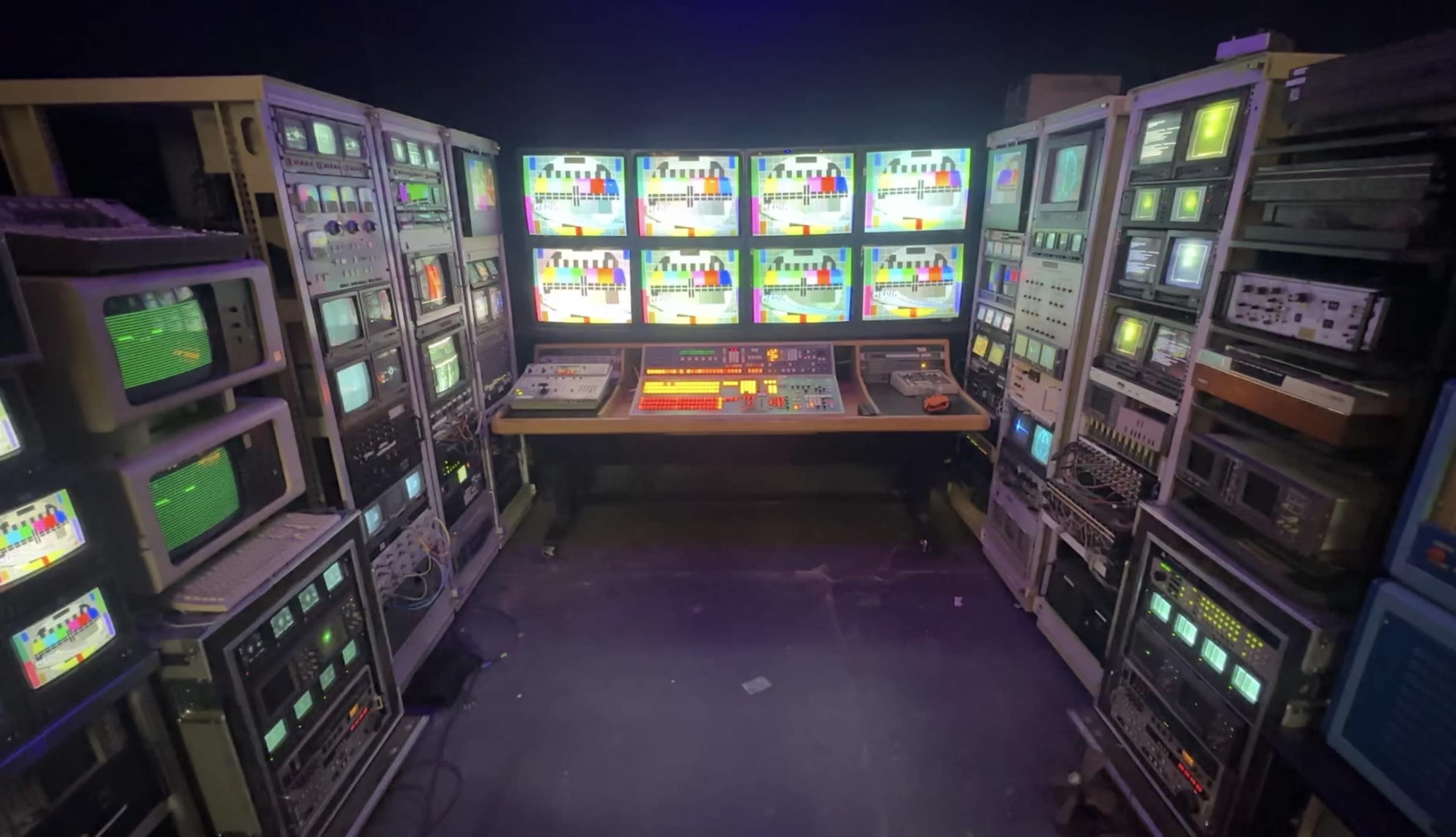The scene shows a retro television studio setup with multiple screens displaying colorful test patterns, surrounded by various broadcasting equipment.