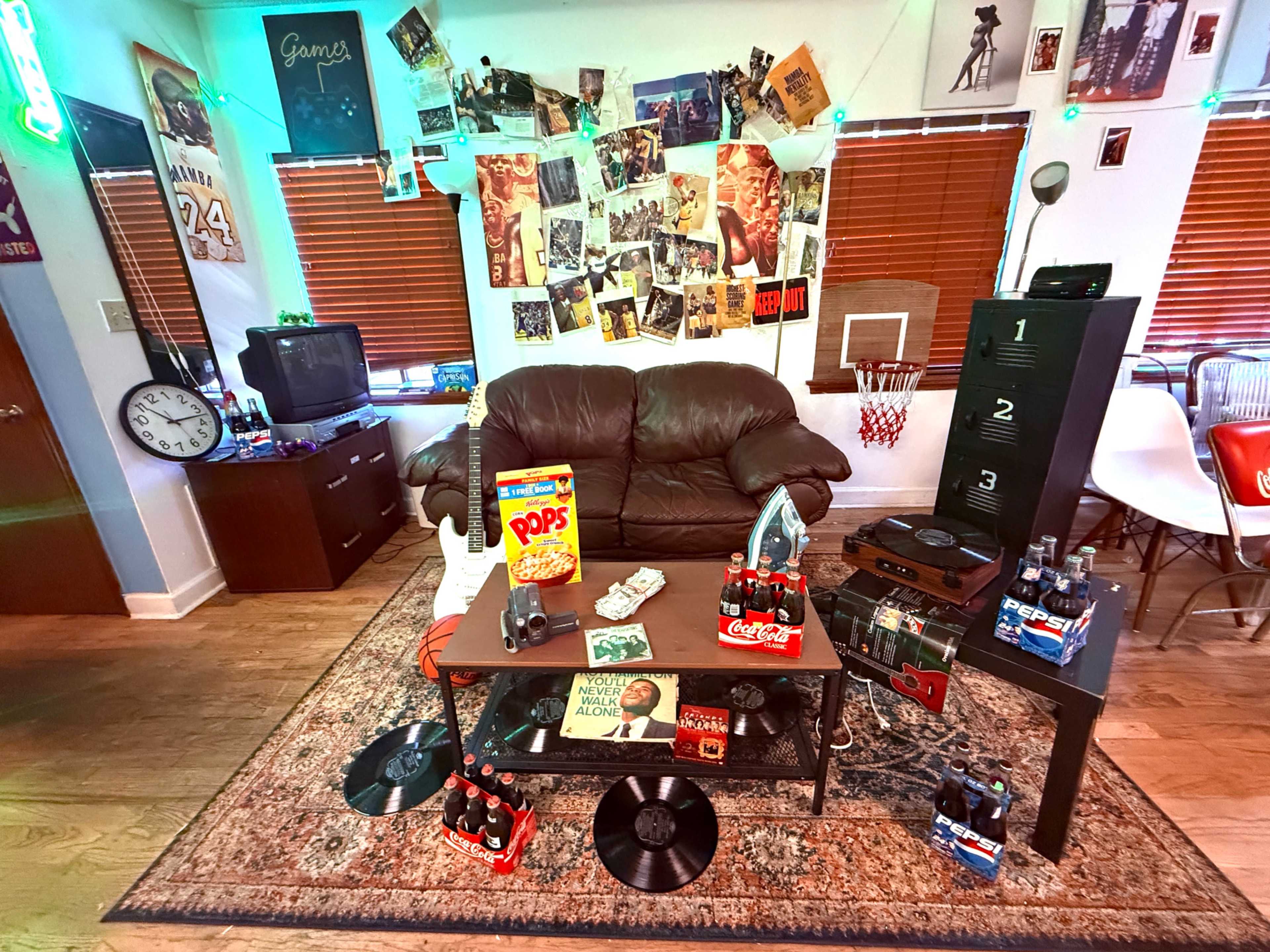 The image depicts a cozy living room filled with vintage decor, featuring a brown couch, a coffee table adorned with records and a cereal box, and walls decorated with posters and photos.