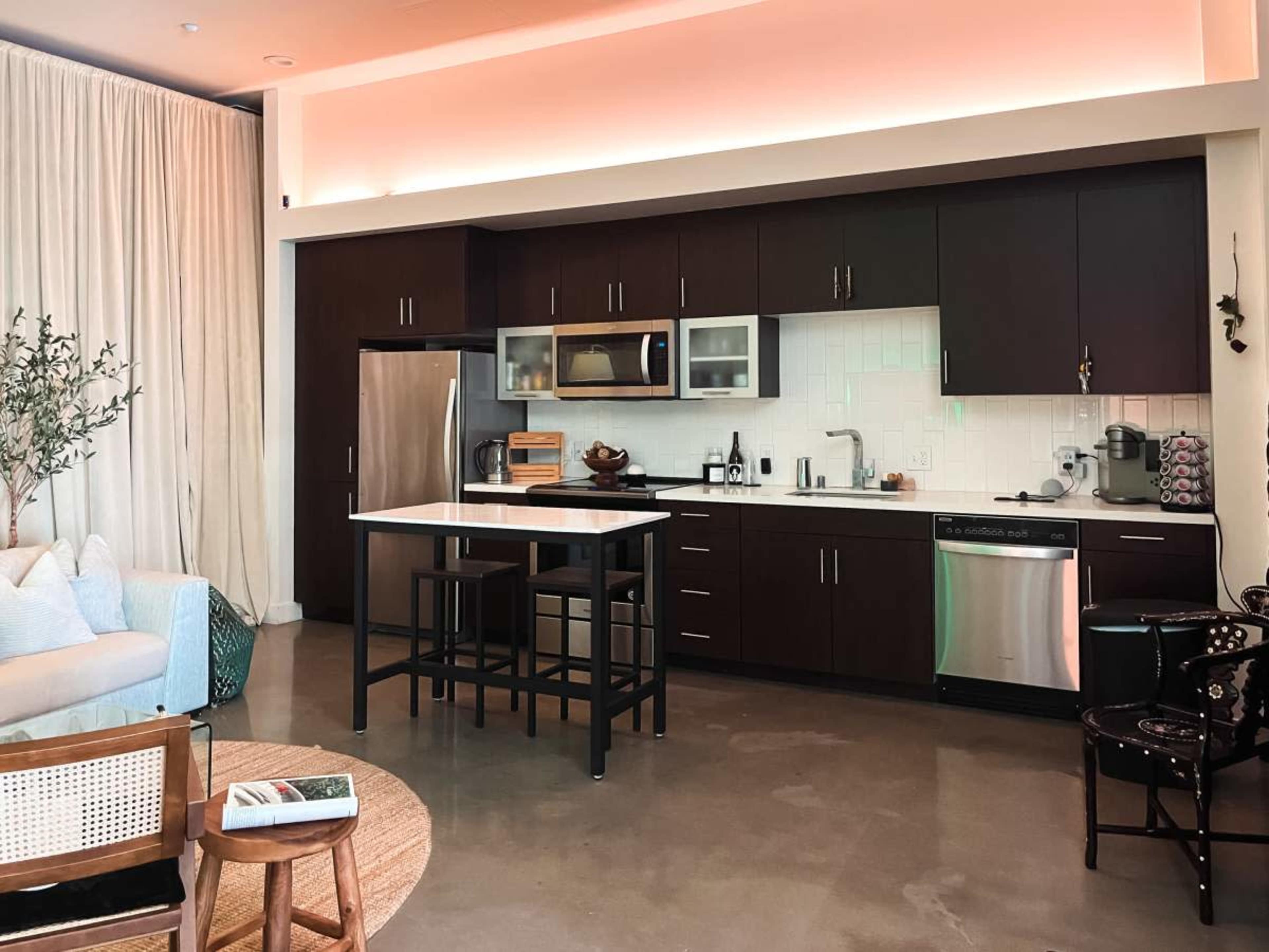 A modern kitchen with dark cabinets, stainless steel appliances, and a central island, accompanied by a seating area.