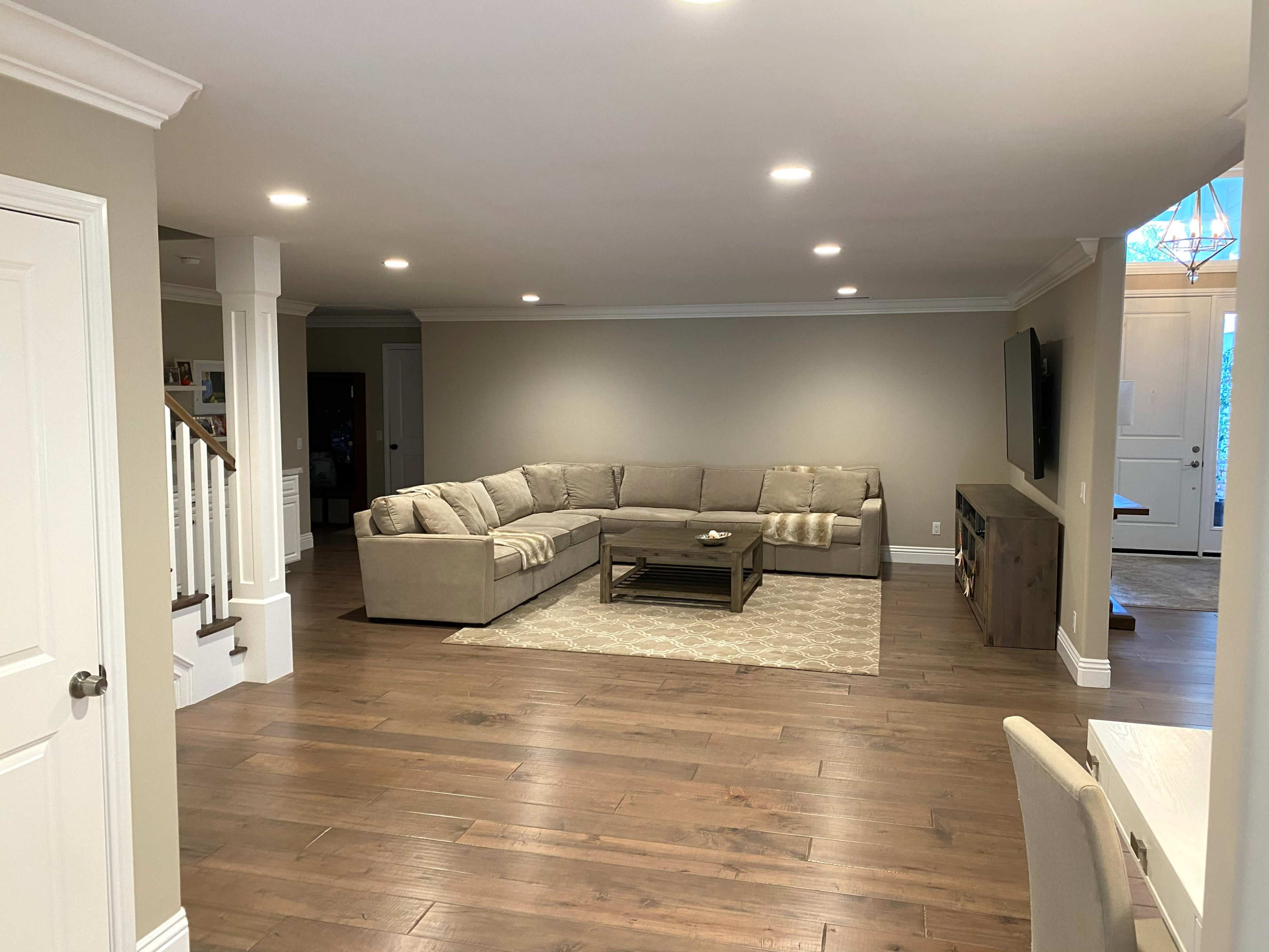 A spacious living room with a sectional sofa, a coffee table, and wooden flooring, illuminated by recessed lighting.