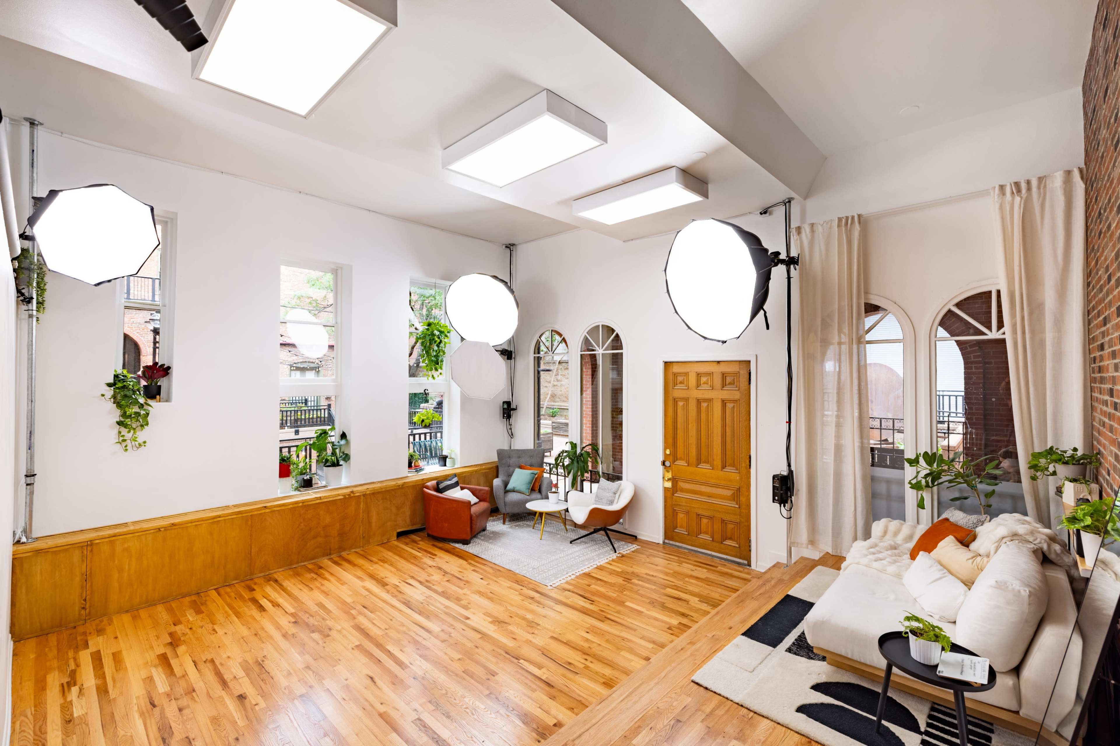 A well-lit interior space features wooden flooring, large windows, and furniture arranged for a cozy seating area.