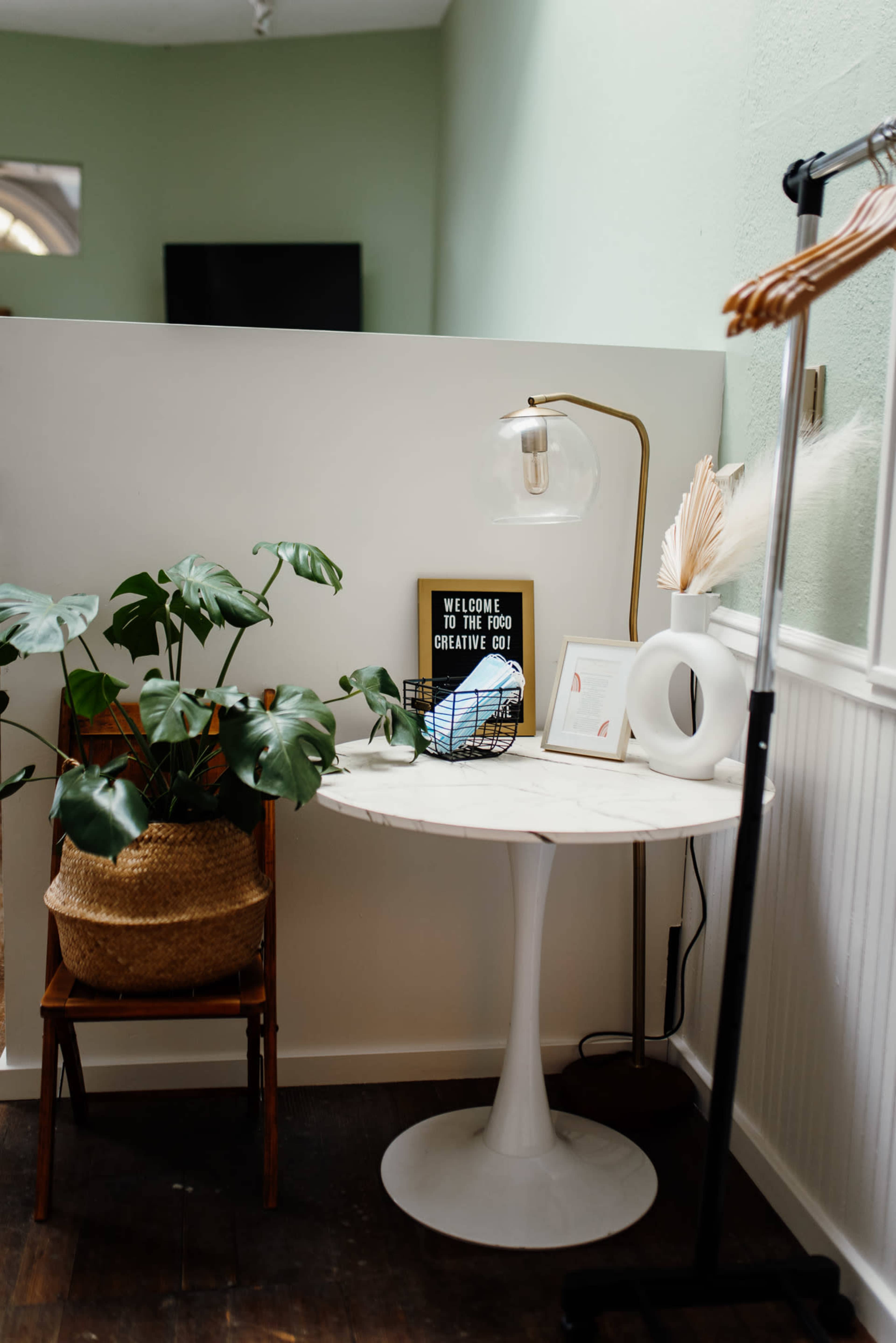 A small table with a plant and a lamp sits next to a wall in a light-colored interior space.