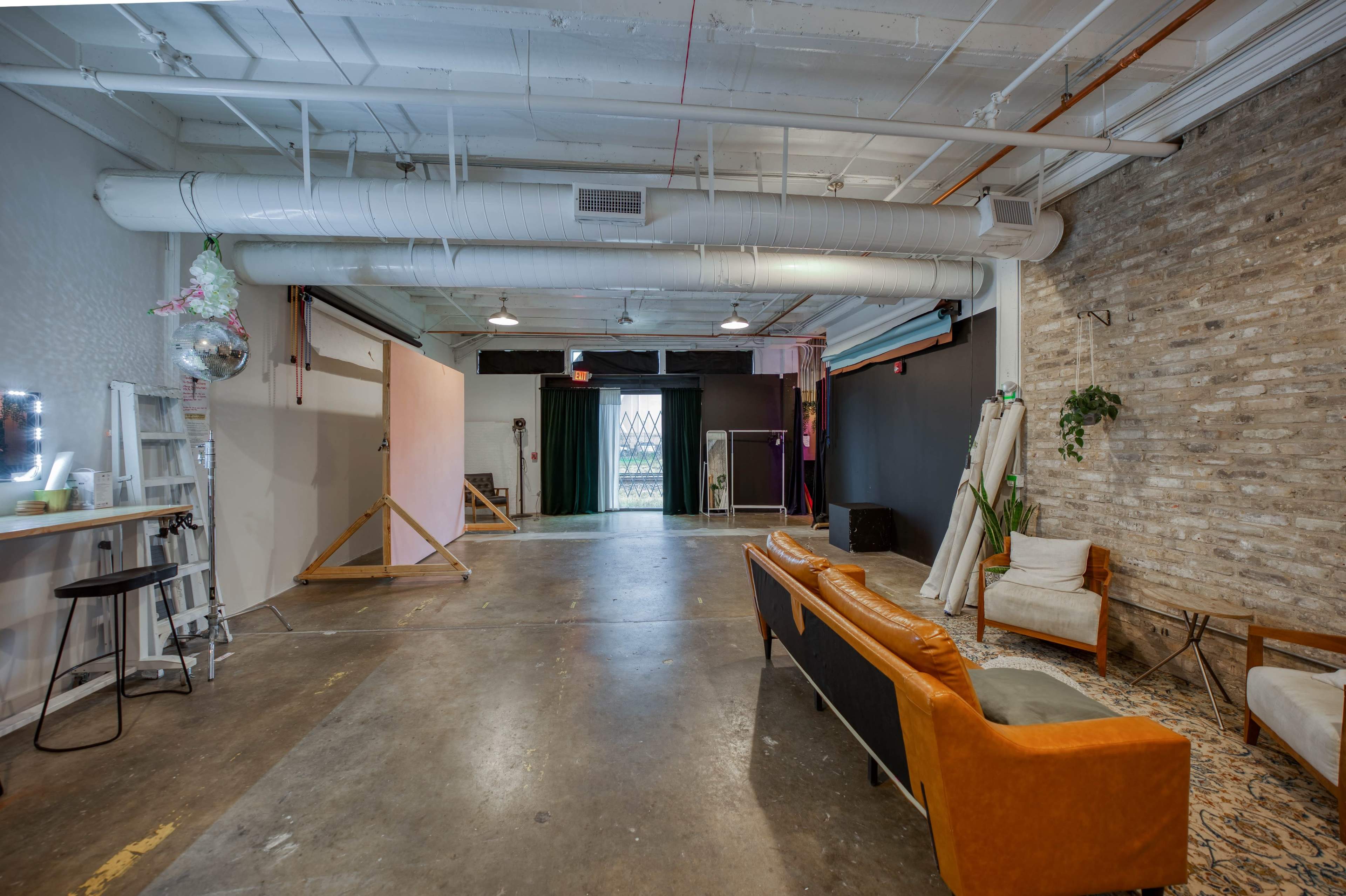 A spacious interior of a studio with a concrete floor, a couch, a chair, and large windows in the background.