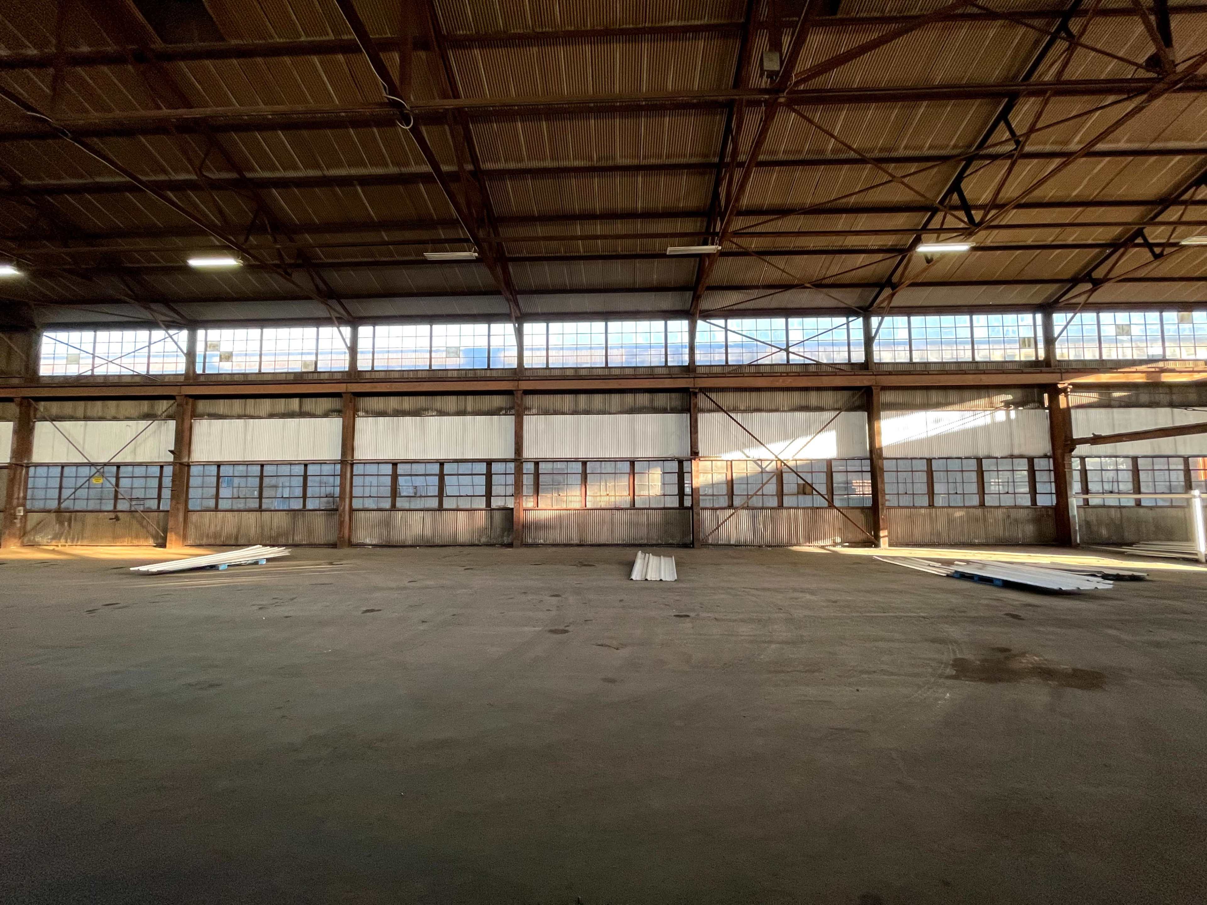 An empty industrial warehouse features large windows along its walls, allowing natural light to illuminate the concrete floor.