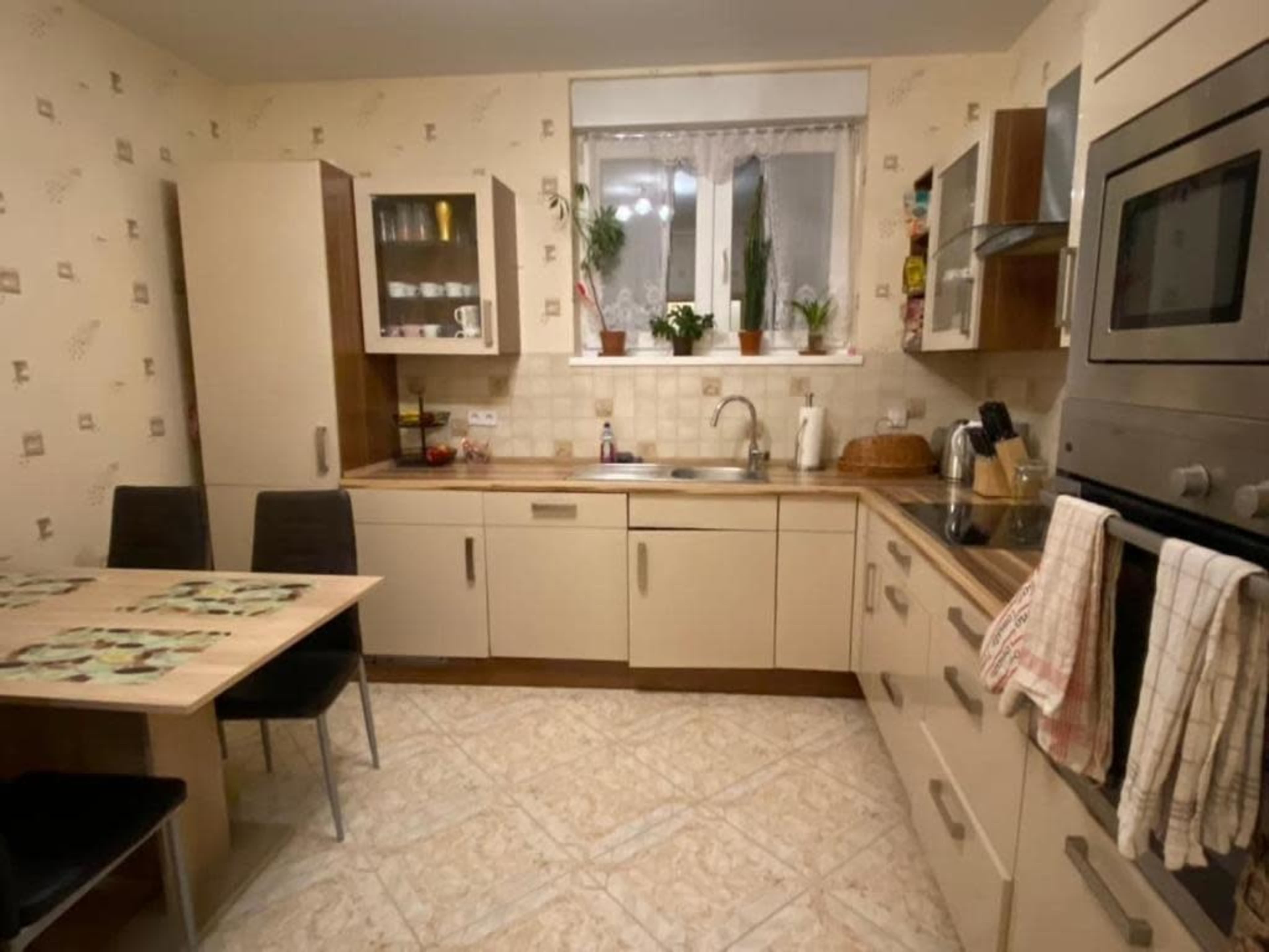 The image shows a kitchen with light-colored cabinetry, a sink, and a small dining table with black chairs.