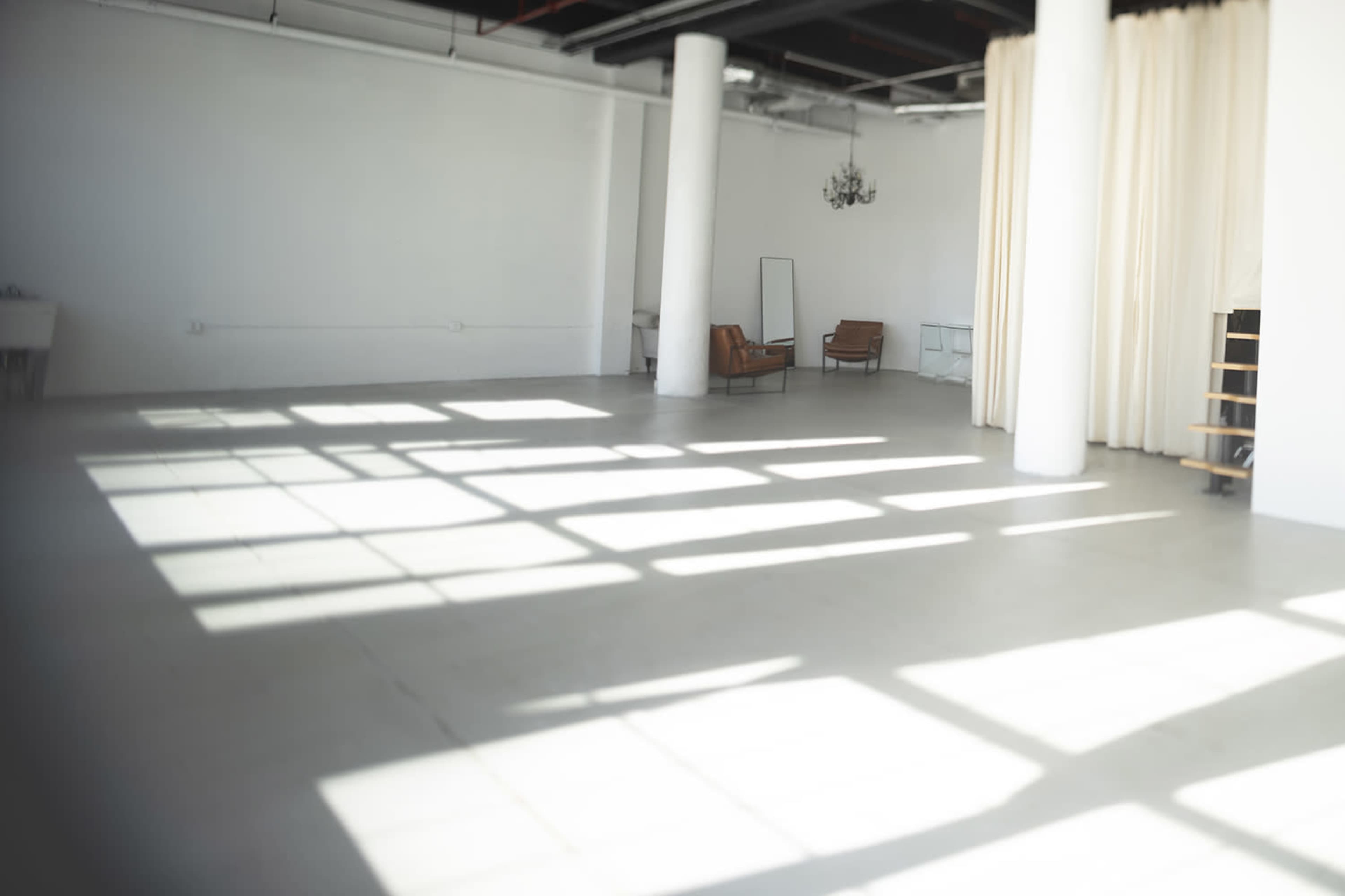 The image depicts a spacious, empty room with white walls and a large window casting shadows across the floor.