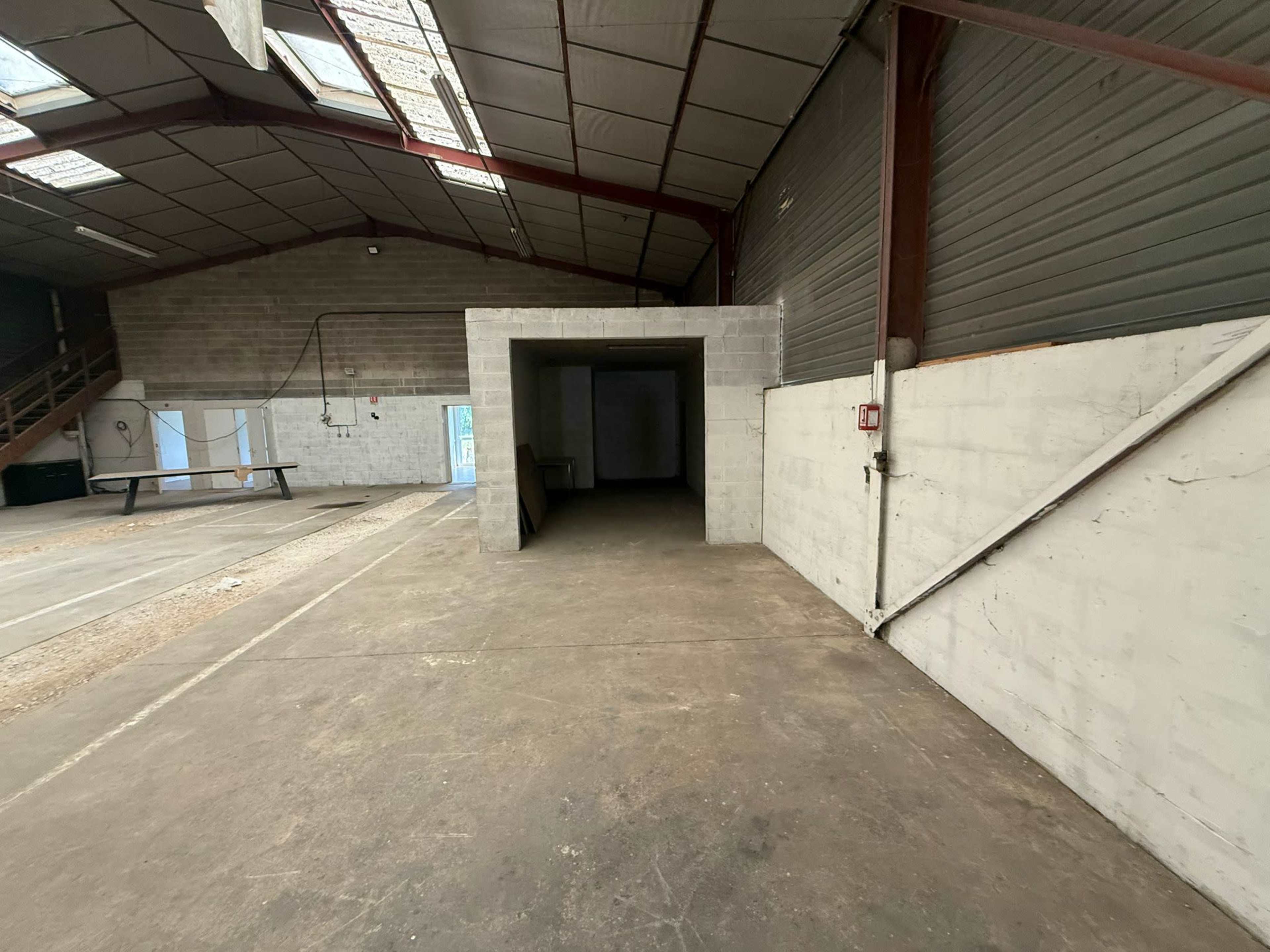 The image shows the interior of a large, empty industrial warehouse with gray concrete walls and a stark, open layout.