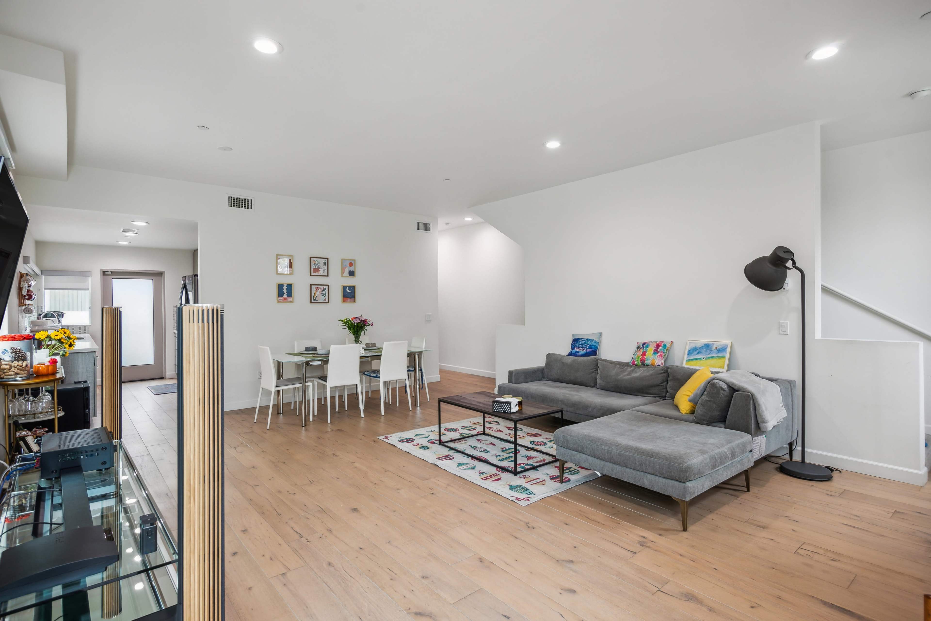 A modern living area with a gray sectional sofa, a coffee table, a dining table with white chairs, and light wooden flooring.