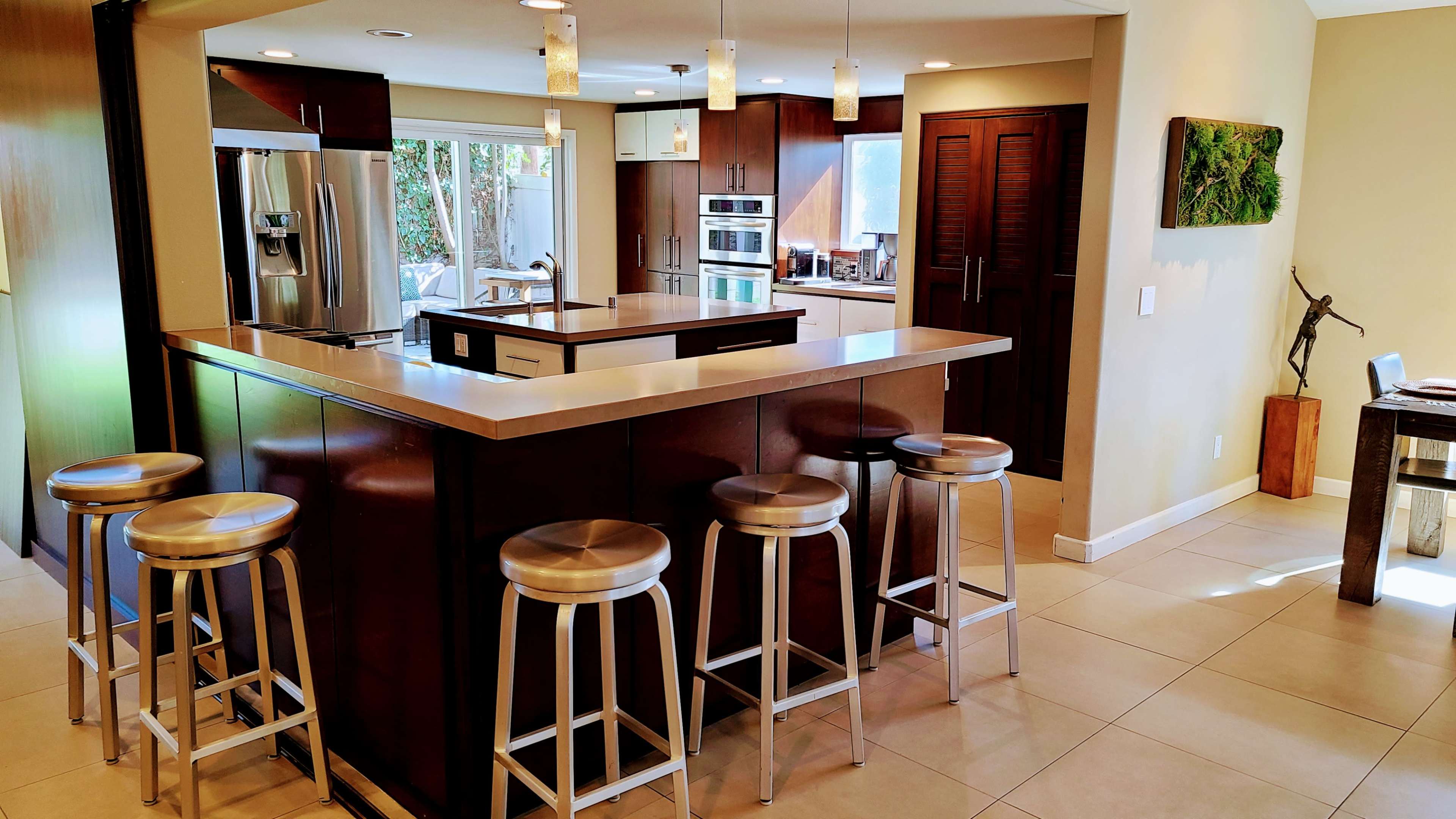 A modern kitchen with dark cabinets, a central island, and metal bar stools arranged around it.