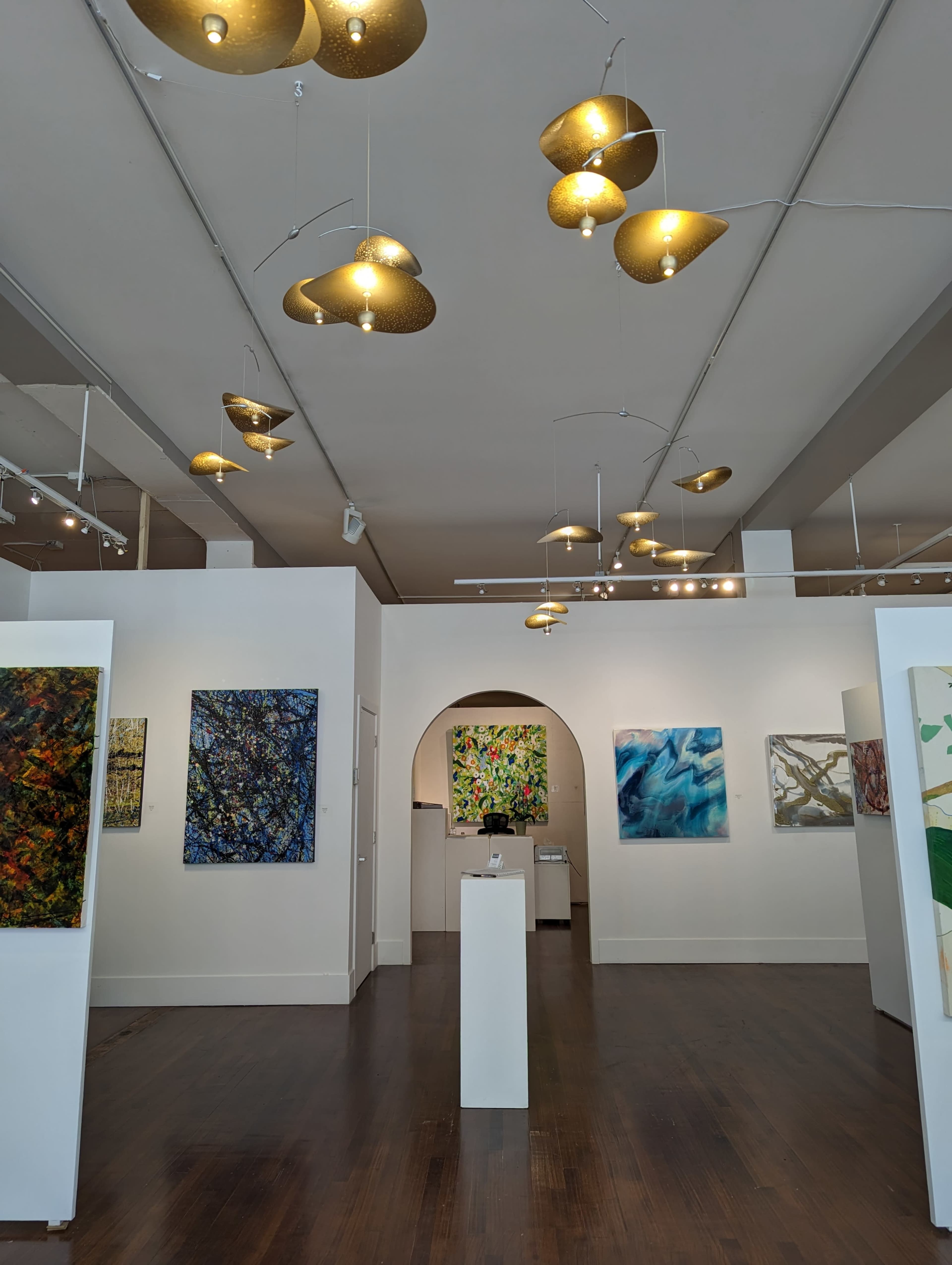 An art gallery featuring several colorful paintings on the walls and hanging light fixtures above.