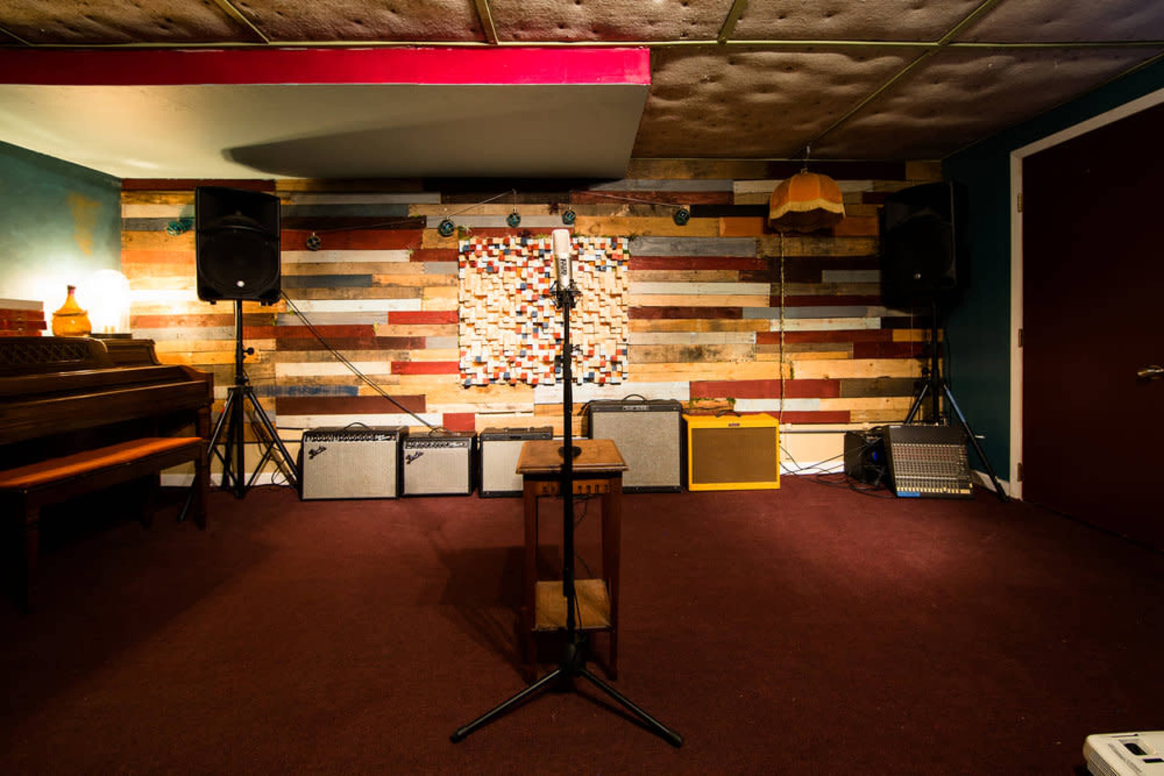 A music performance space featuring a microphone stand in front of amplifiers and a colorful wooden wall.