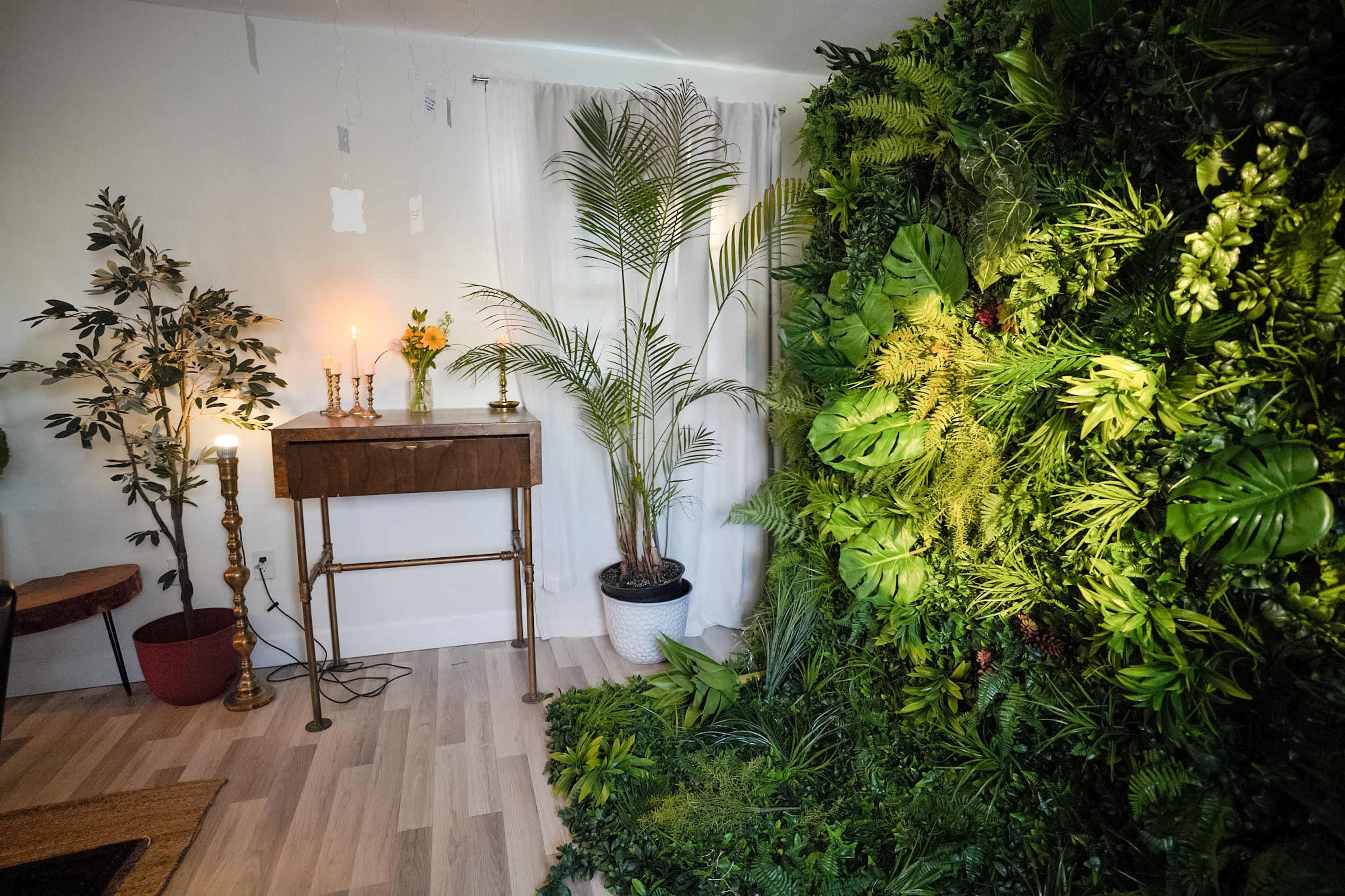 The image shows a room with a vertical garden wall, a small wooden table with candles, and a potted plant beside it.