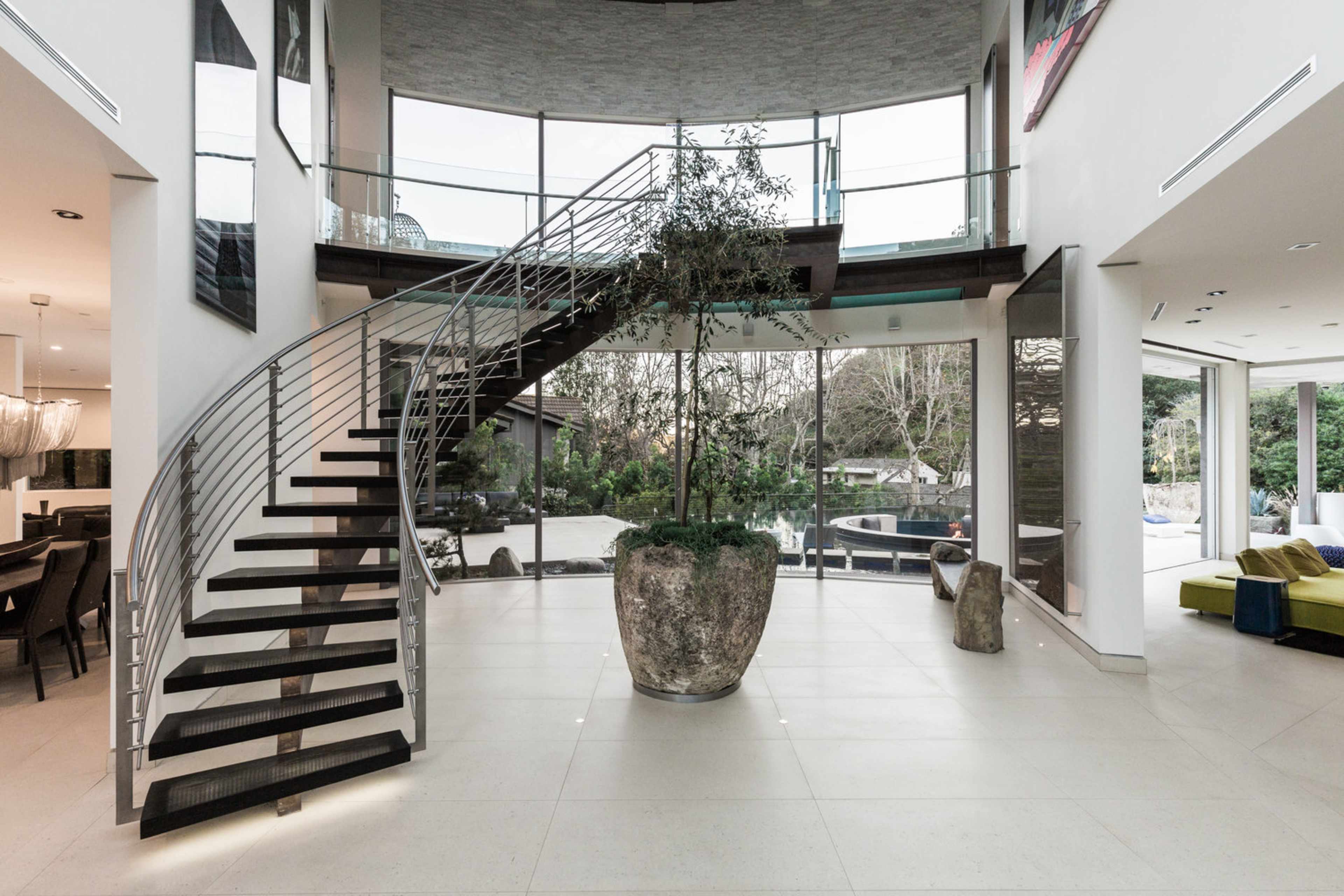 A modern entryway with a spiral staircase, large glass windows, and an indoor plant in a stone planter.